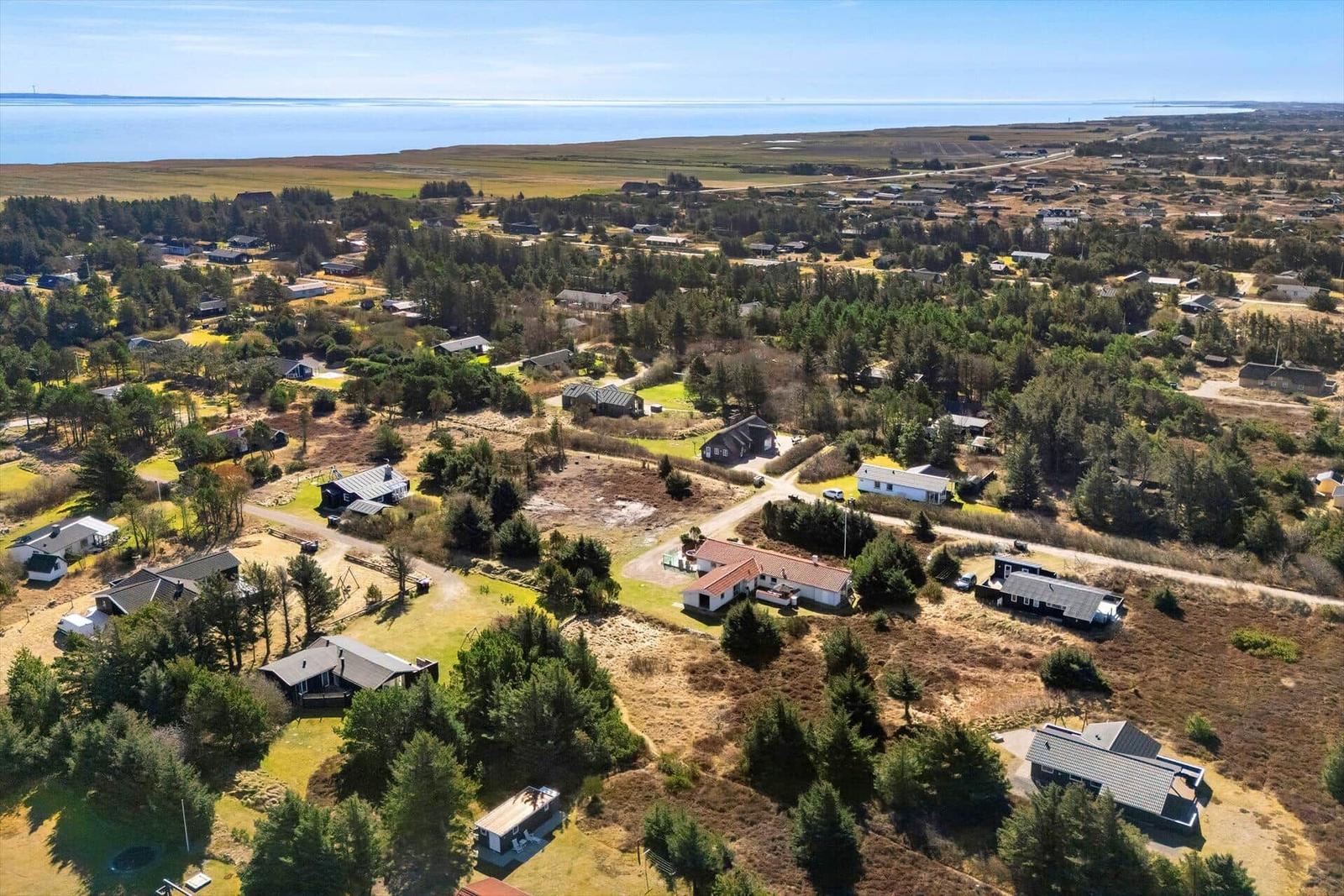 Luftbild von Wohnhäusern in einer ländlichen Gegend mit Wald und Meer im Hintergrund.