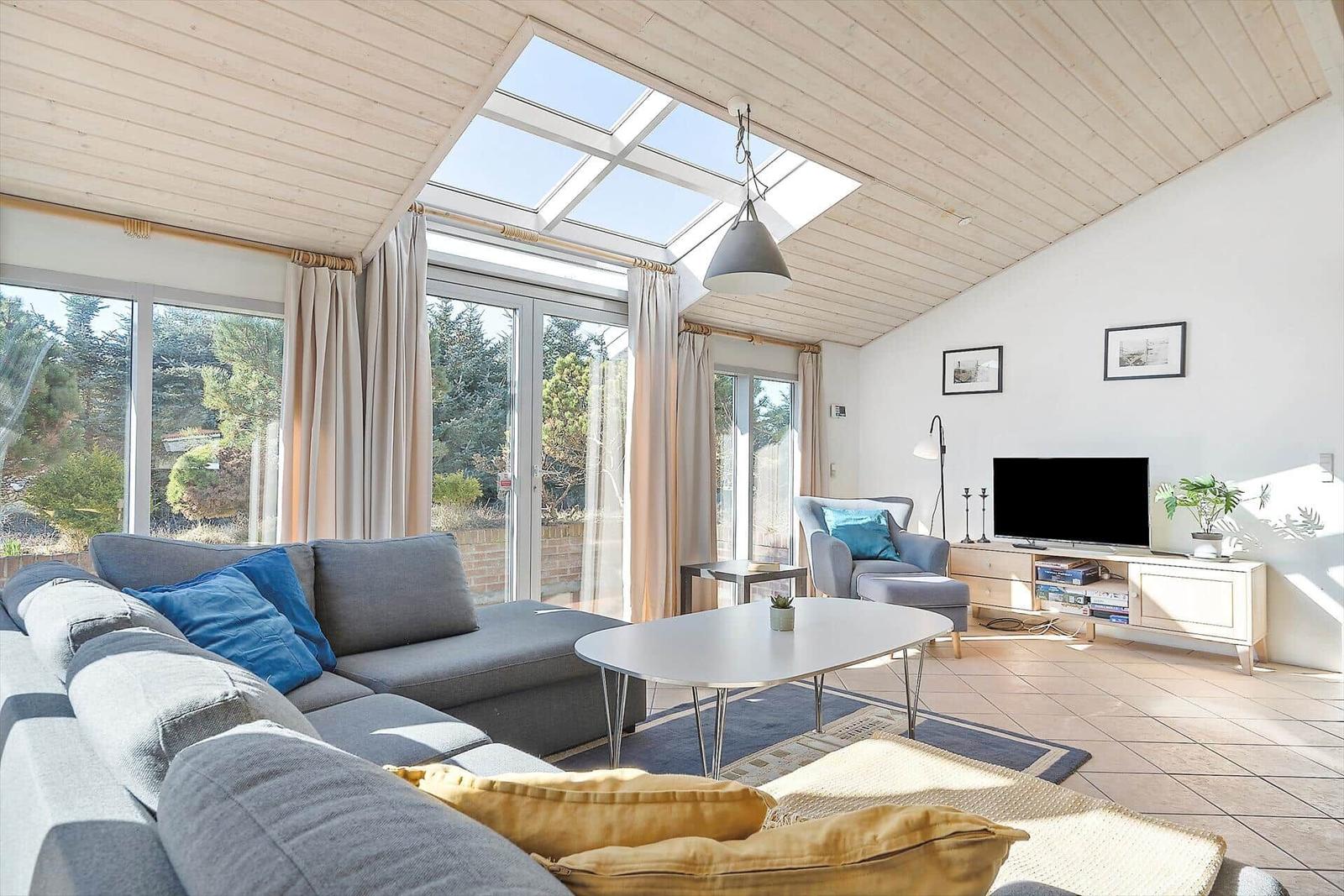 Wohnzimmer mit Sofa, Couchtisch und TV. Große Fenster und Dachfenster.