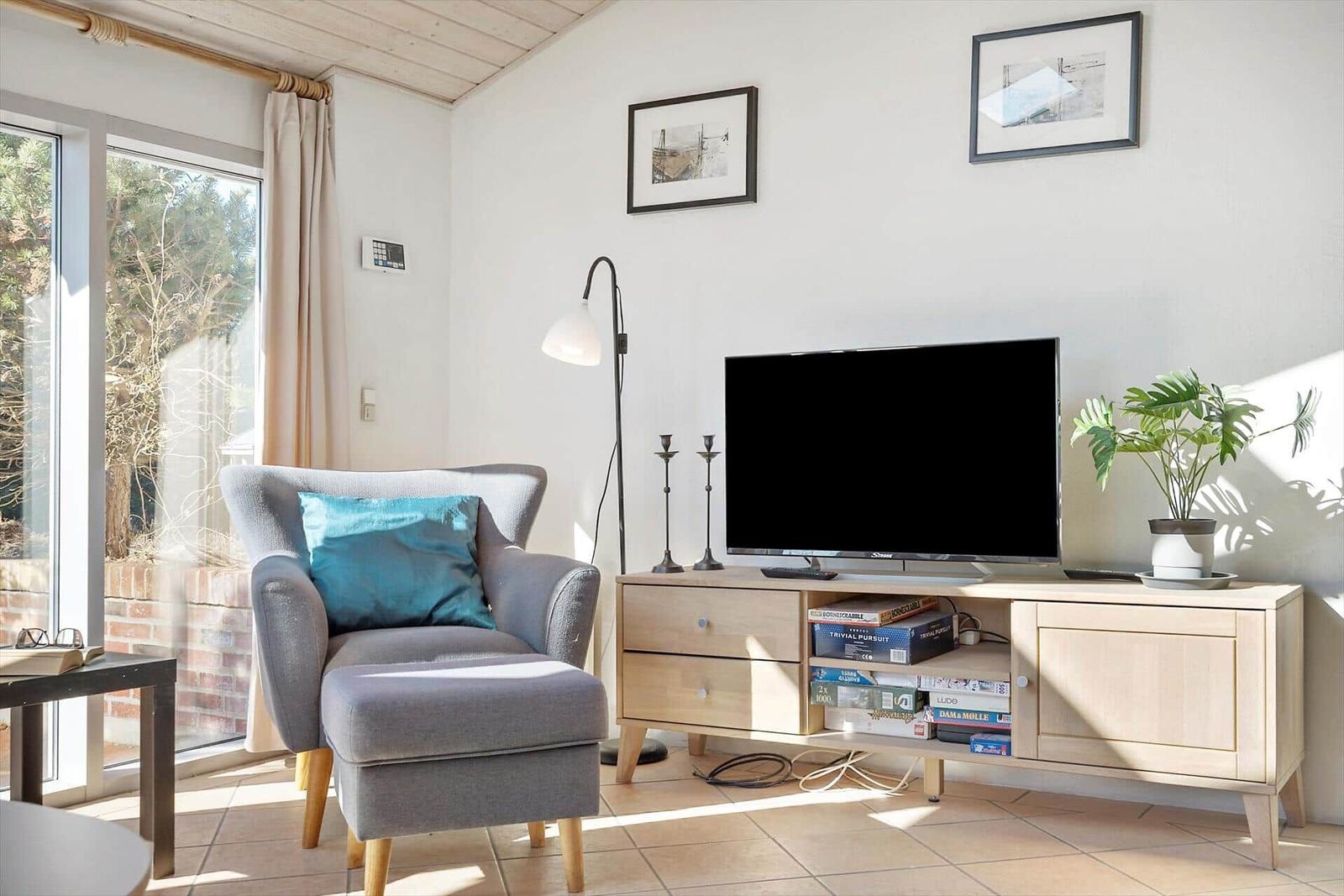 Ein Wohnzimmer mit grauem Sessel, Fernseher und Holzmöbeln.