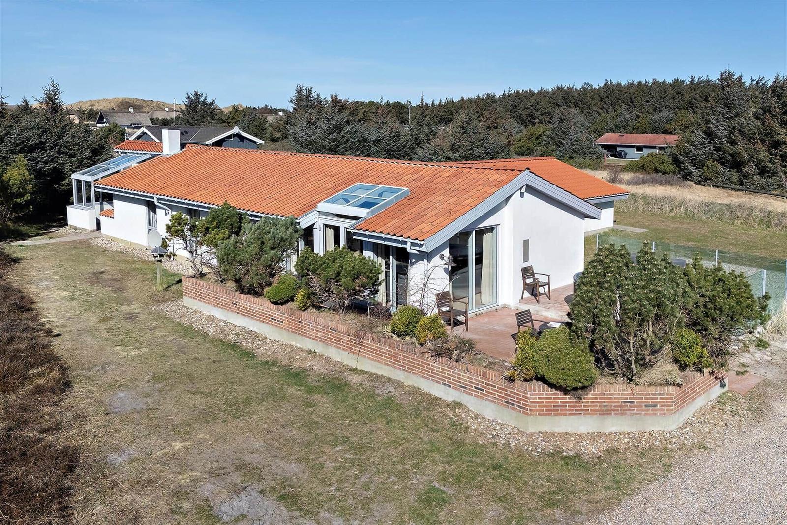 Moderne Villa mit rotem Dach und Terrasse. Umgeben von Grün und Wald.