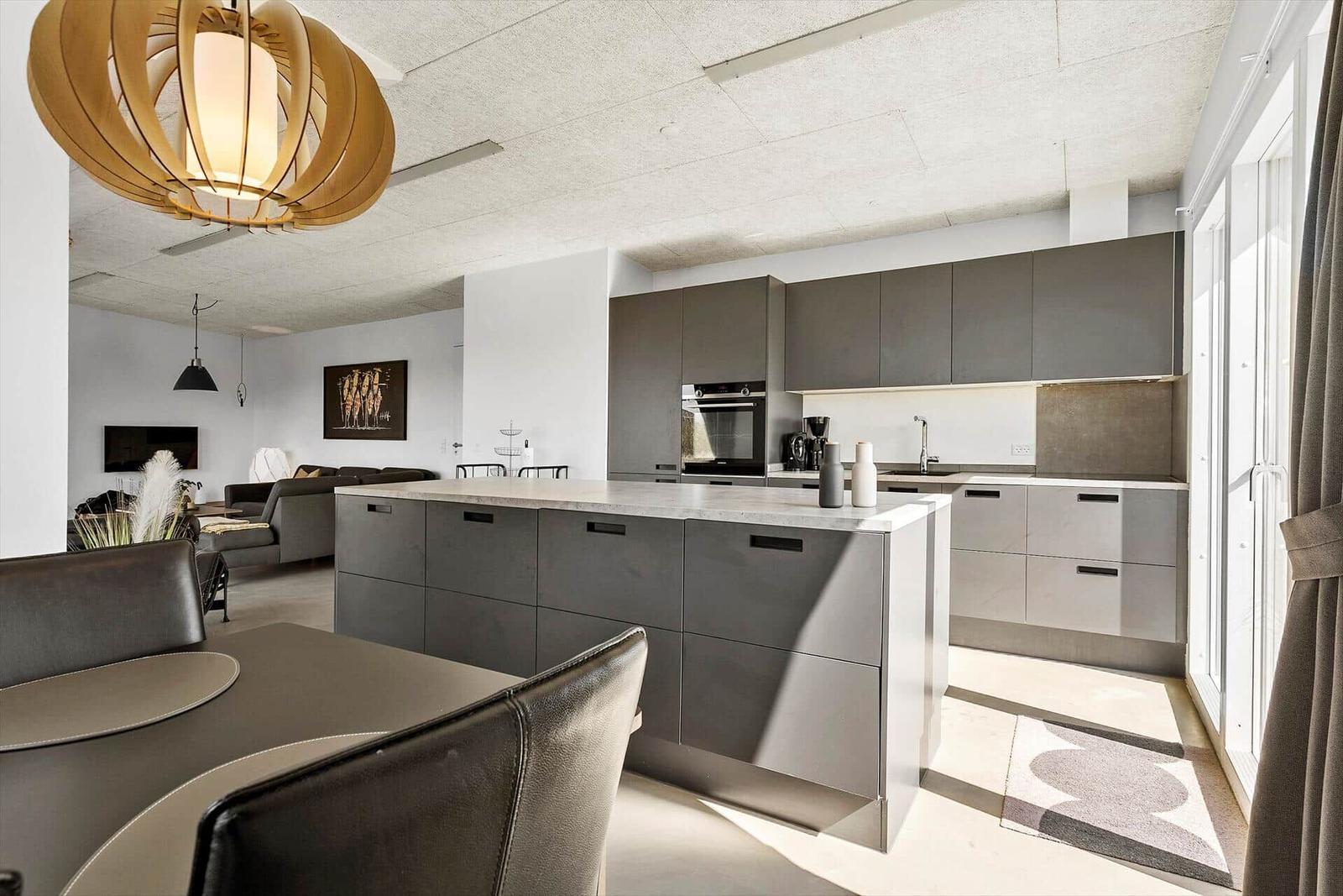 Moderne Küche mit Kücheninsel, grauen Schränken und Essbereich im Hintergrund.