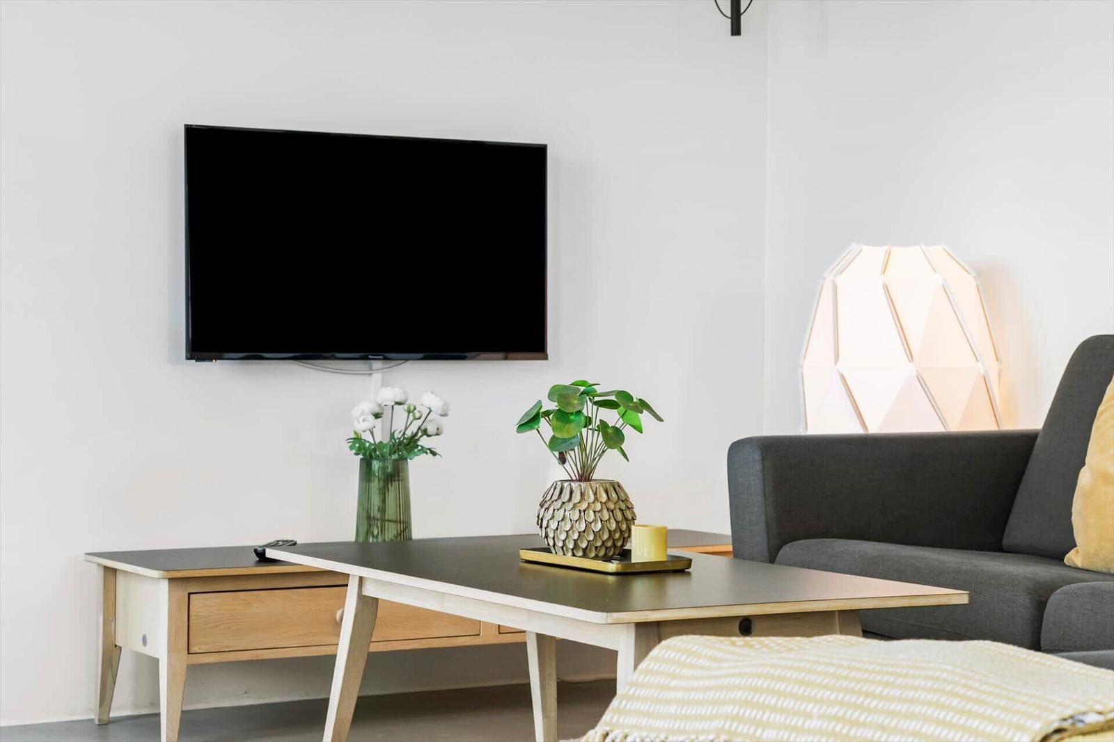 Wohnzimmer mit Sofa, Couchtisch, Fernseher und Pflanzen.