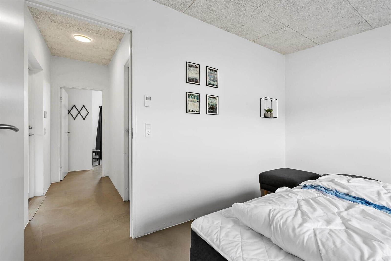 Schlafzimmer mit Bett, Wandbildern und Bodenbelag. Durchgang zur nächsten Tür.