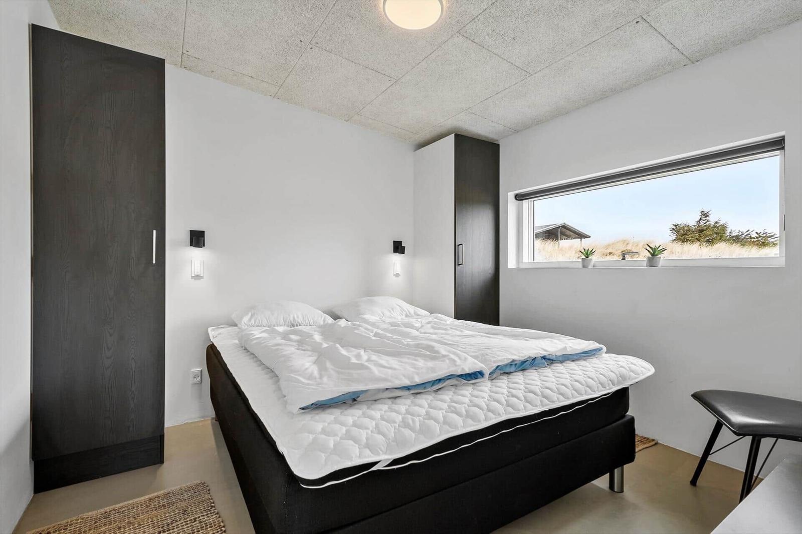 Schlafzimmer mit Bett, Kleiderschränken und Fensterblick auf Grasland.