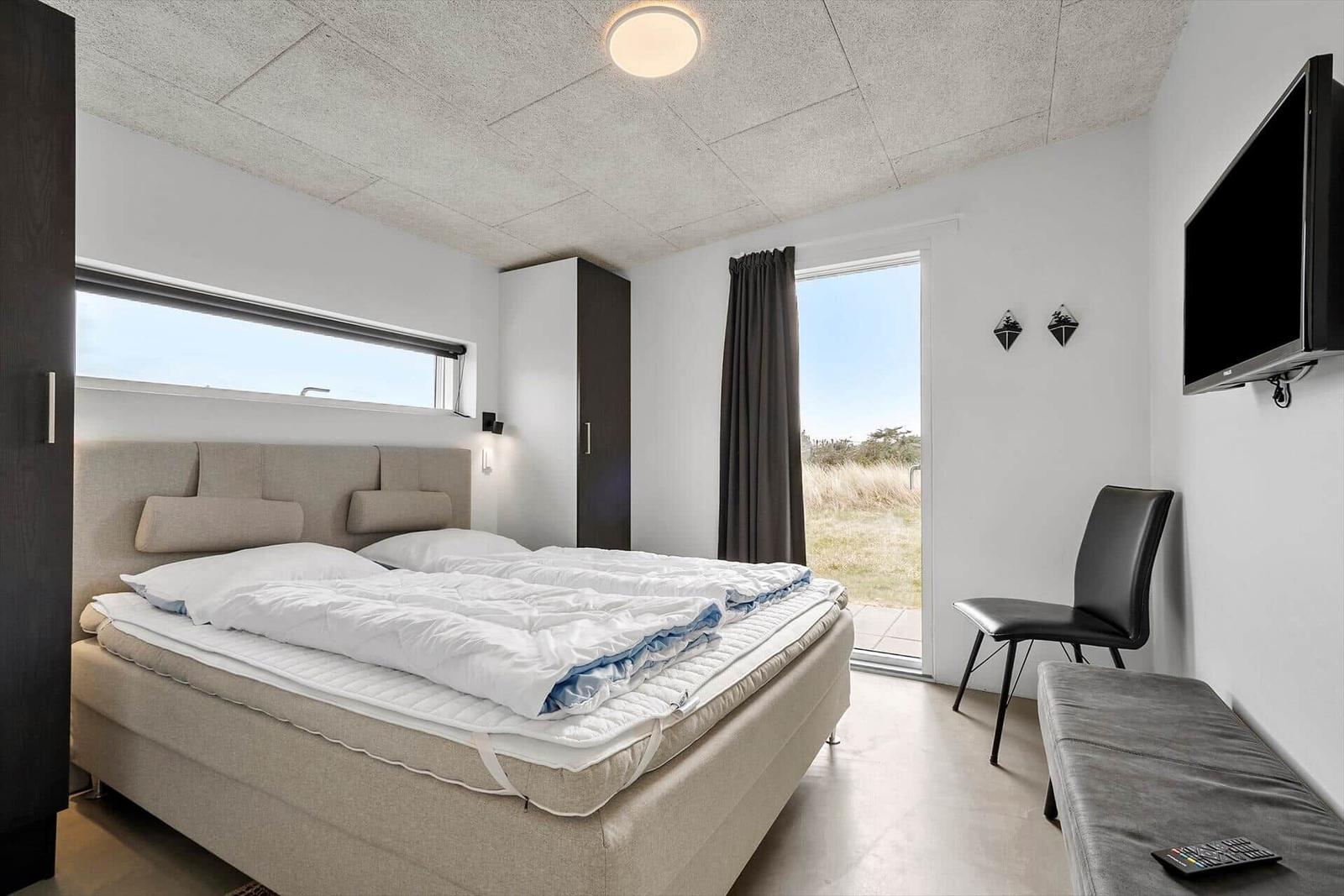Schlafzimmer mit Doppelbett, TV und Blick auf die Außenterrasse.