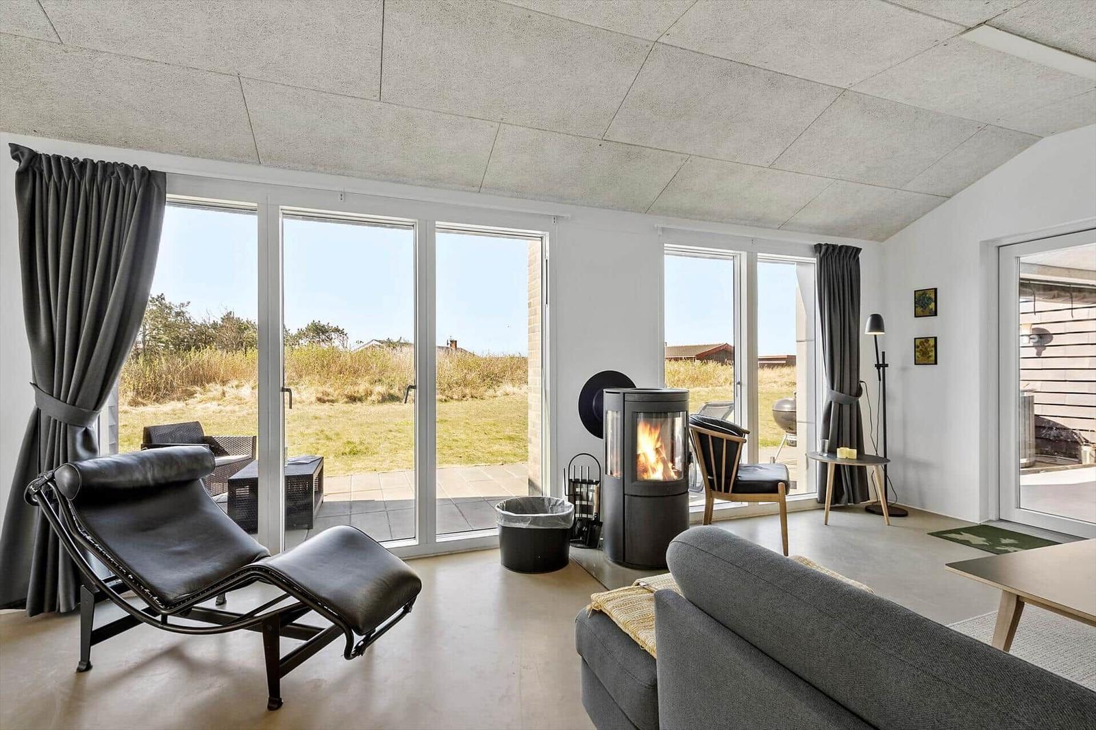 Wohnzimmer mit Kamin, Sofa und Liege. Große Fenster und Terrasse.