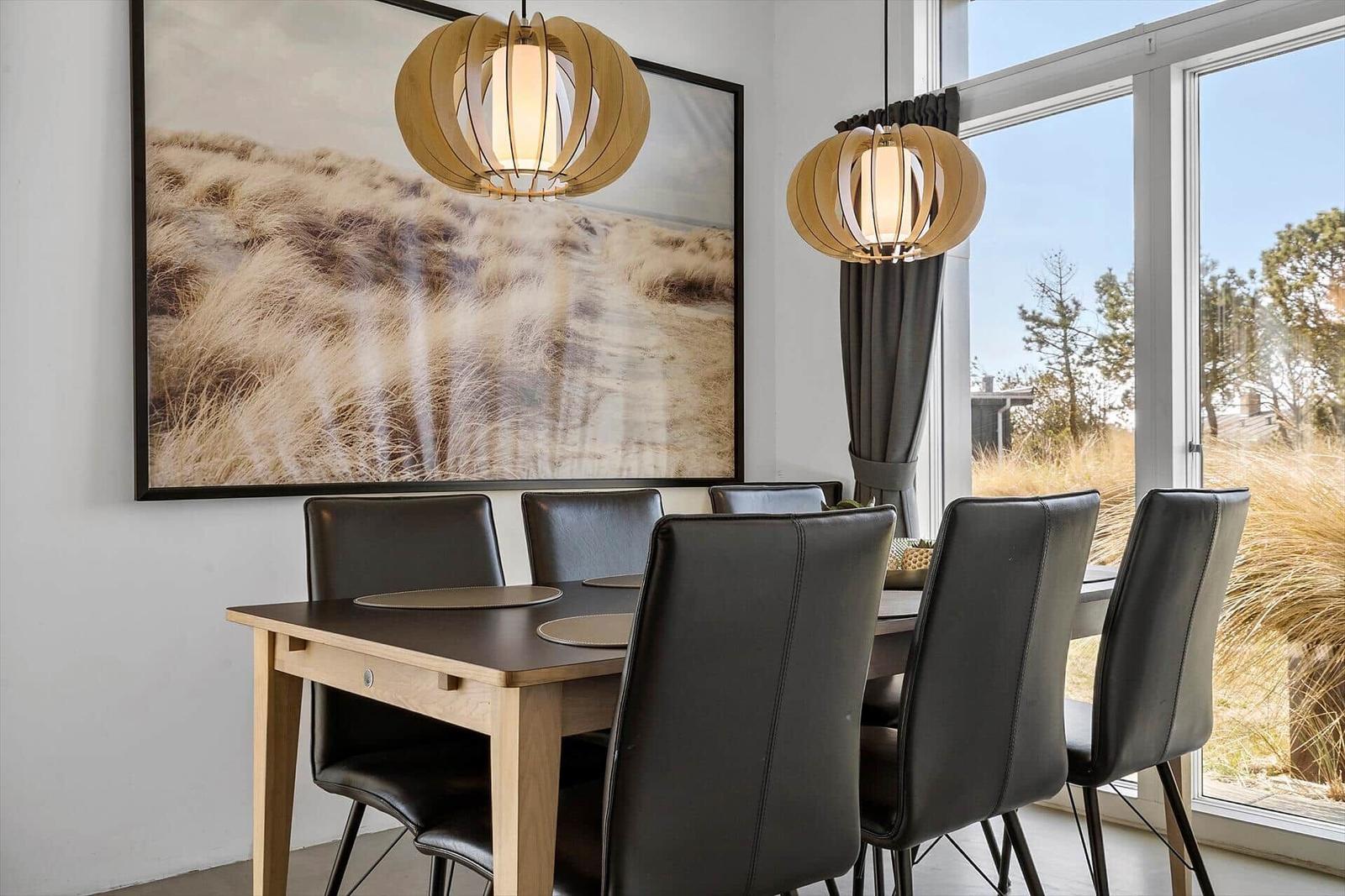 Esszimmer mit Tisch, Stühlen und großen Fenstern. An der Wand hängt ein großes Bild.