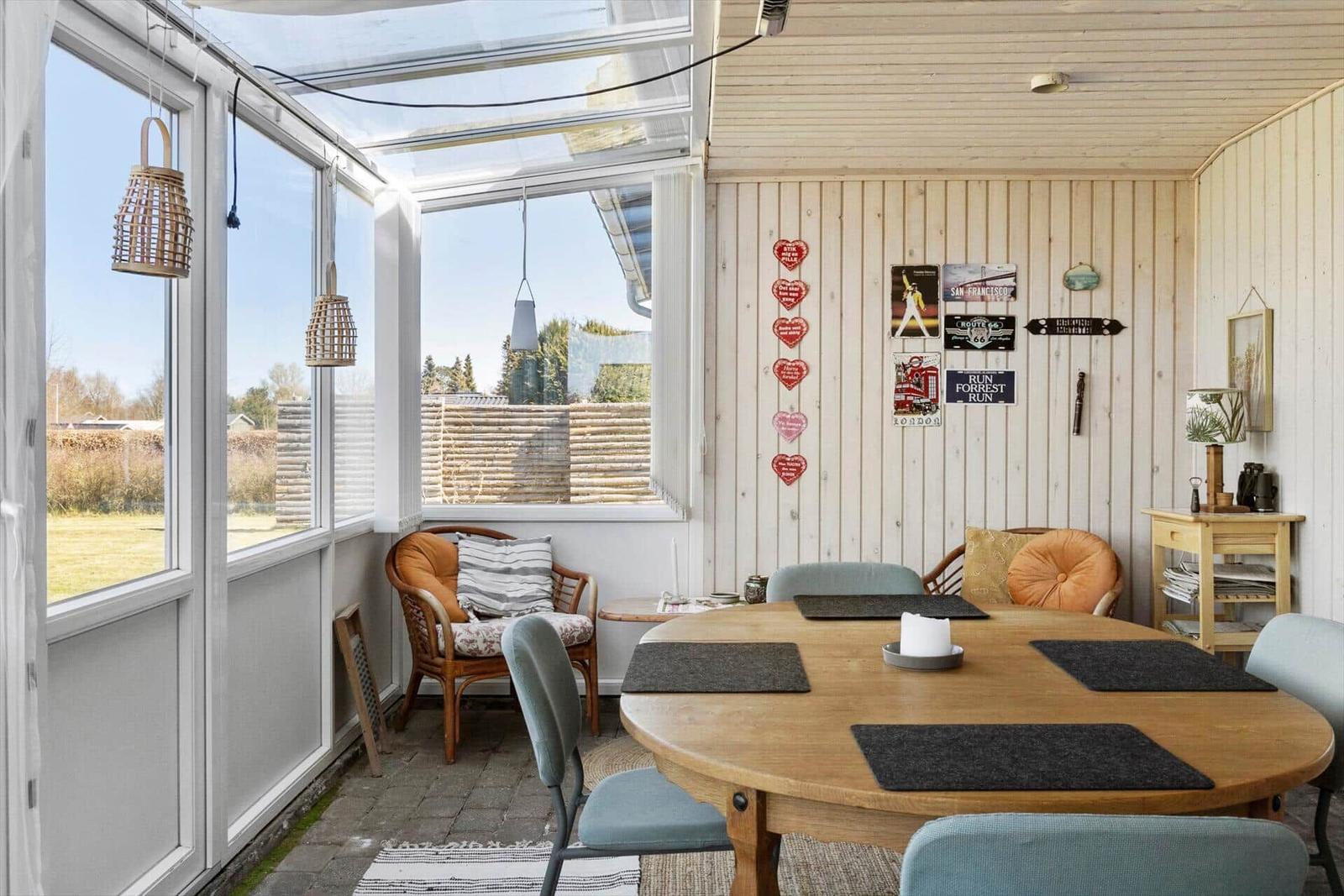 Terrassenbereich mit Holztisch, Stühlen und Fenstern. Wand mit Dekoration.