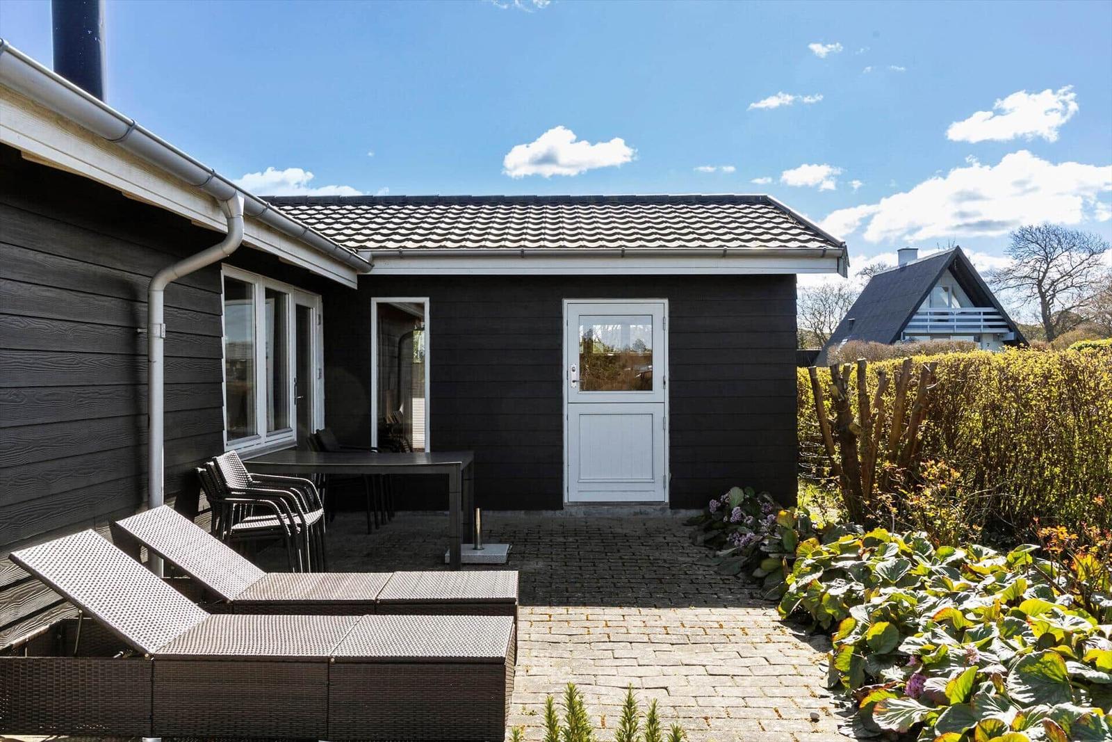 Haus mit Terrasse, Garten und weißer Tür unter blauem Himmel.