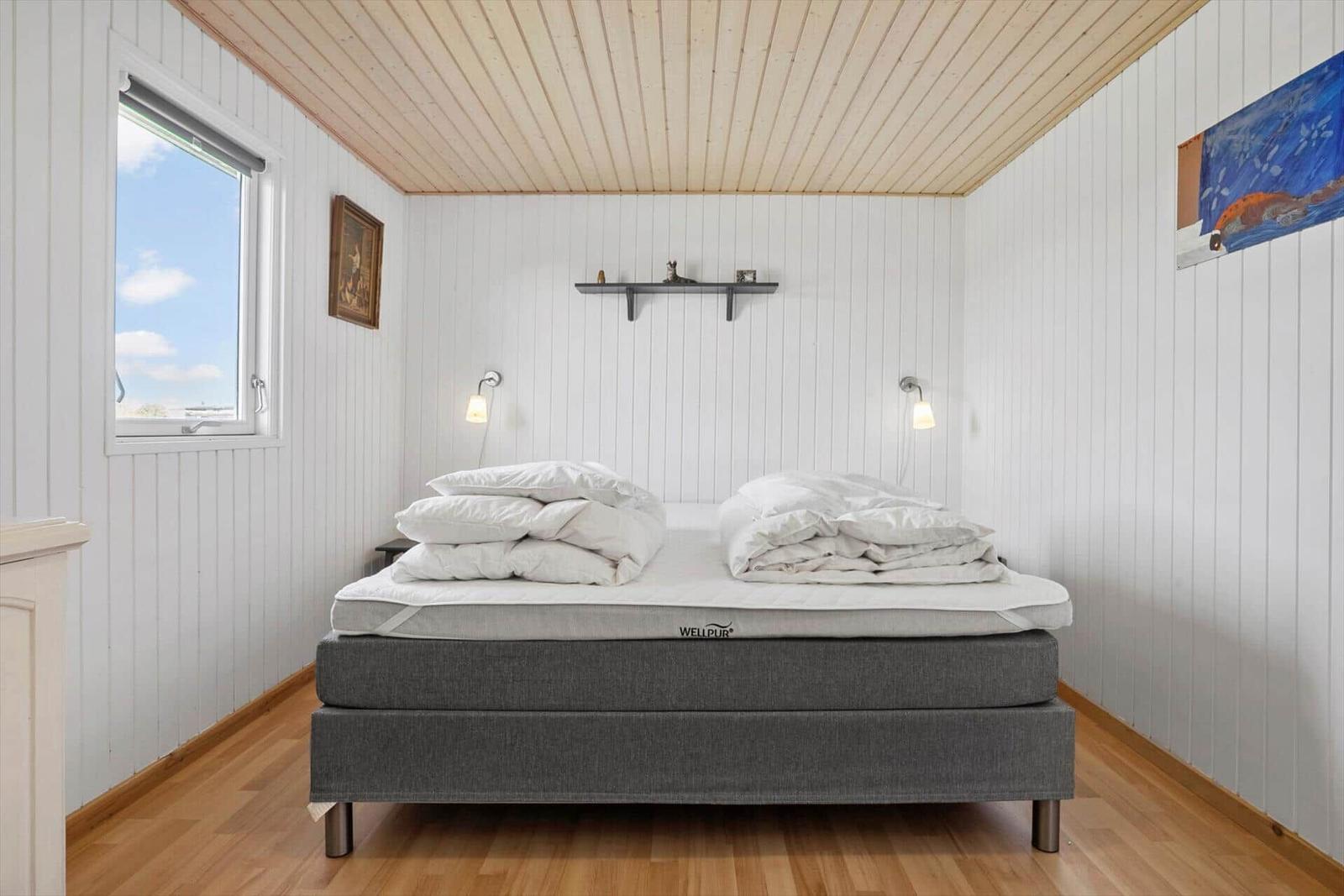 Schlafzimmer mit Bett, Fenster und Wandregal.