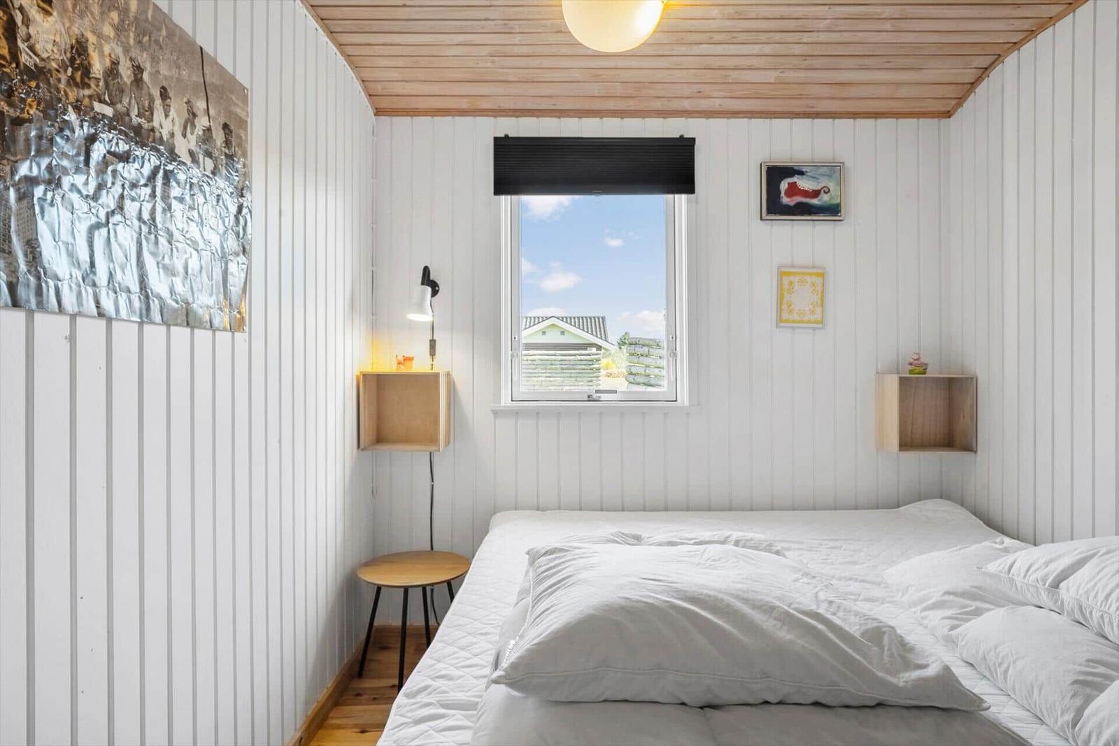 Schlafzimmer mit weißem Bett, Holzdecke und Fenster mit Blick auf Außenbereich.