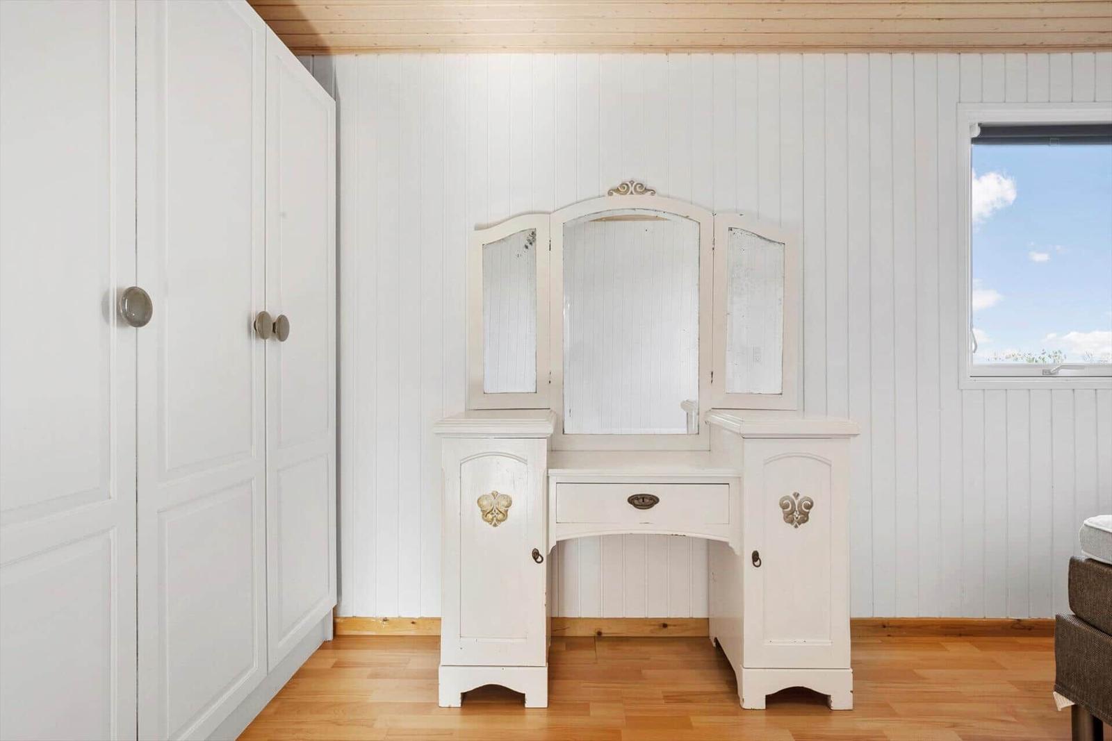 Schminktisch mit Spiegeln und Schublade vor weißer Wand.
