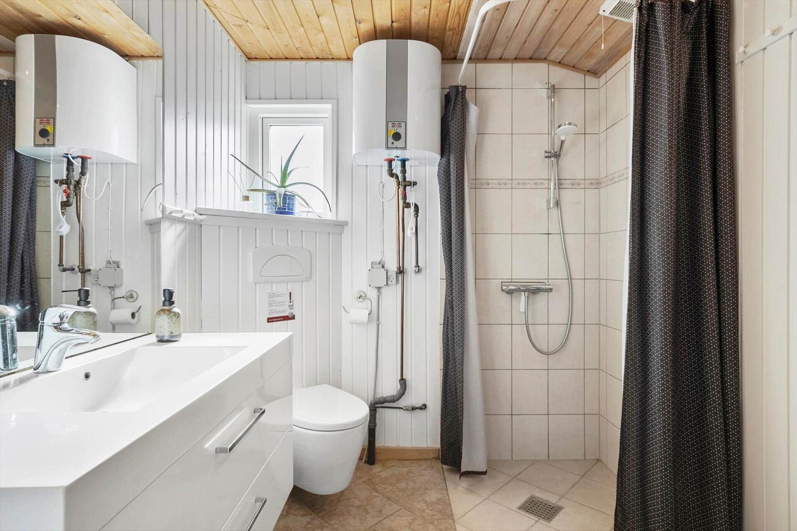 Badezimmer mit Dusche, Waschbecken und Toilette. Holzdecke und weiße Wände.