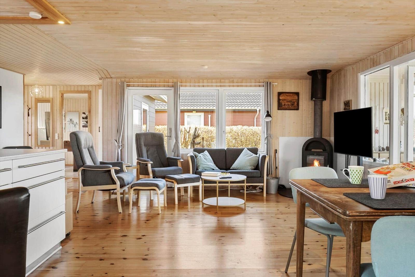 Wohn- und Essbereich mit Kamin, Sofa und Stühlen. Holzboden und -decke.