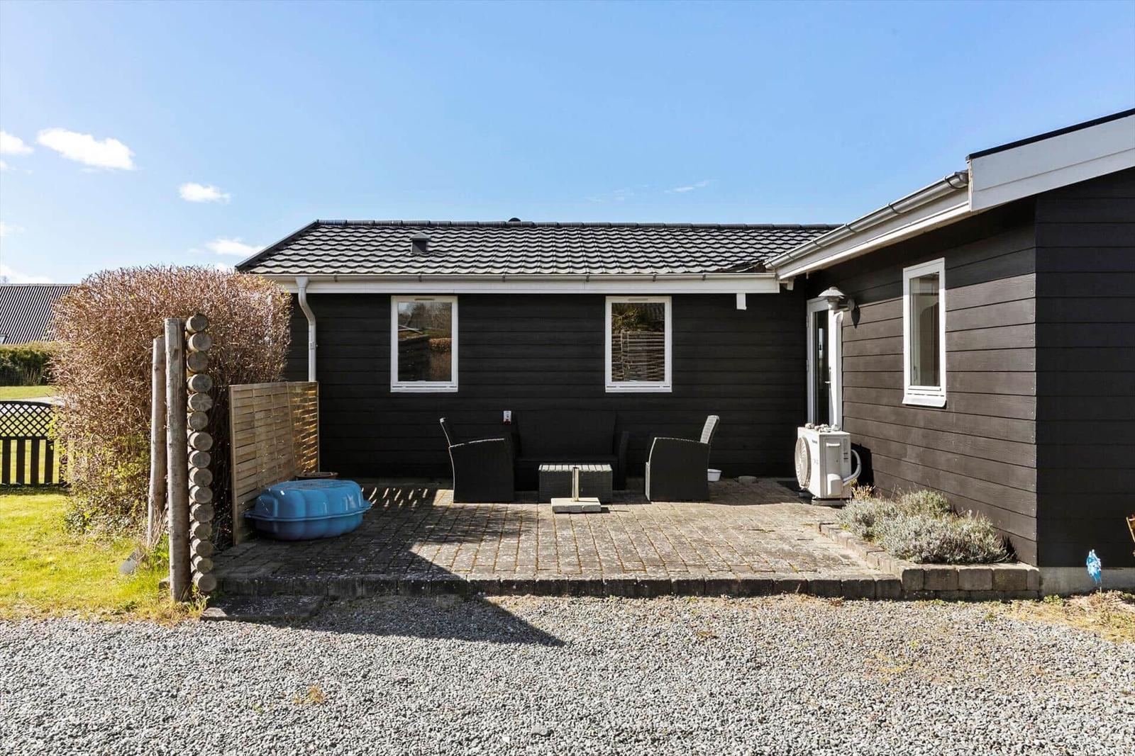 Schwarzes Haus mit Terrasse, Sitzmöbeln und blauem Pool. Gras und Steinplatten.