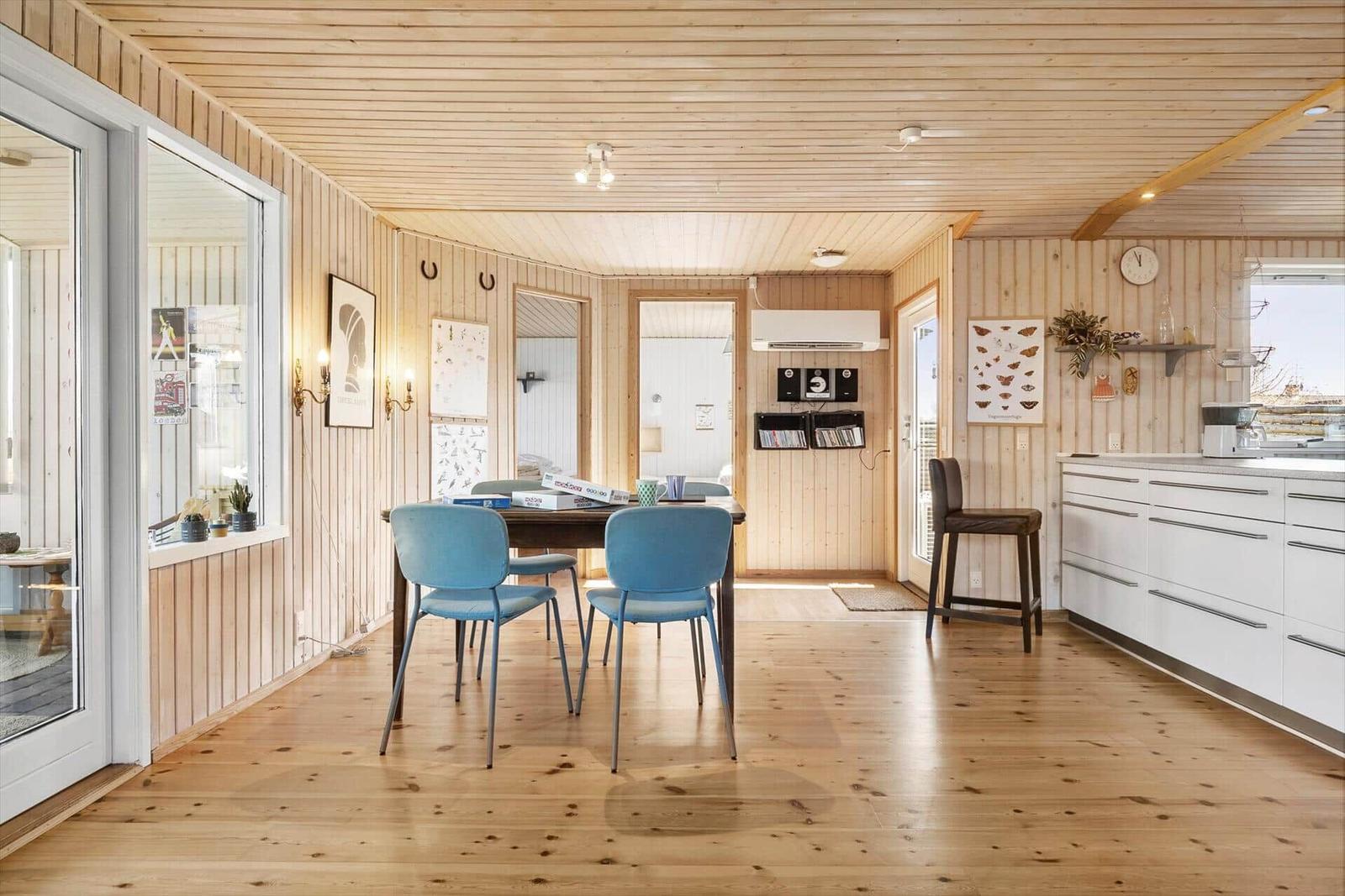 Holzvertäfelte Küche mit Esstisch, blauen Stühlen und Fensterblick.