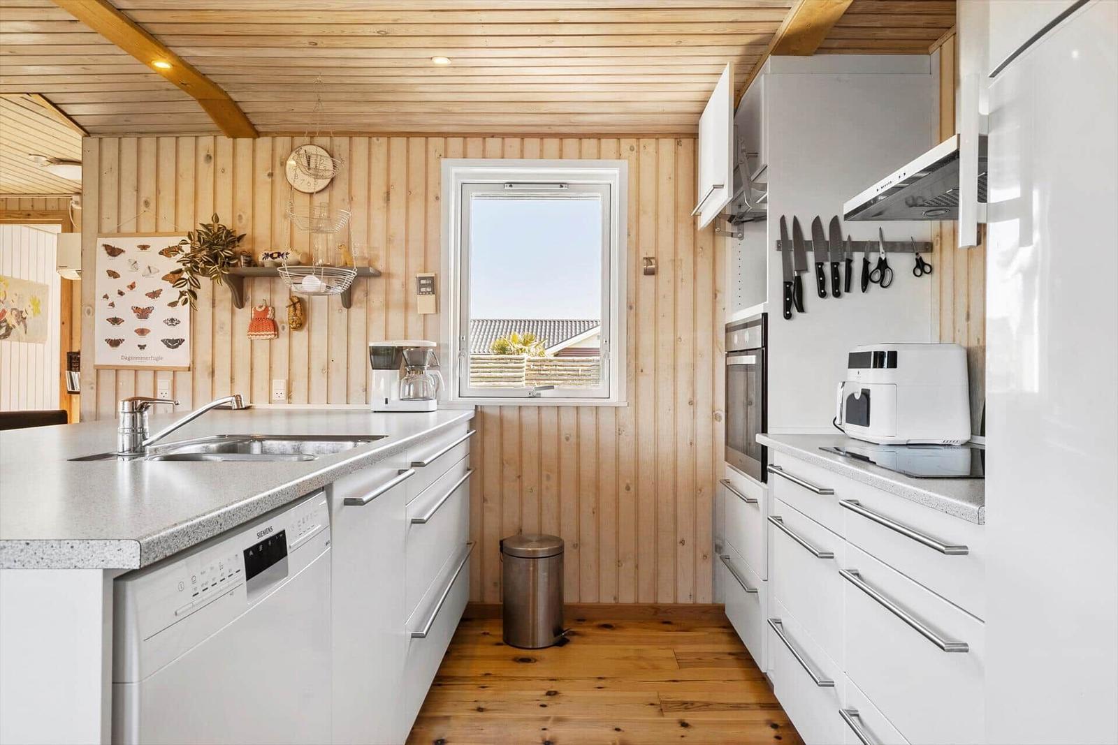 Küche mit weißen Schränken, Holzwand und Fenster zum Garten.