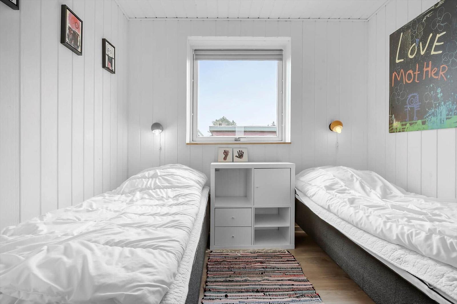 Two beds with white bedding are in a room with white walls and a window.