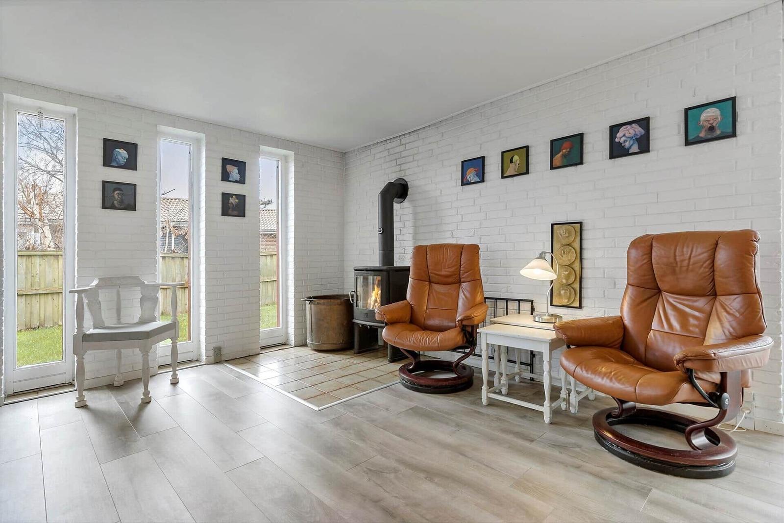 Two brown leather chairs, fireplace and wall art in a room with white brick walls.