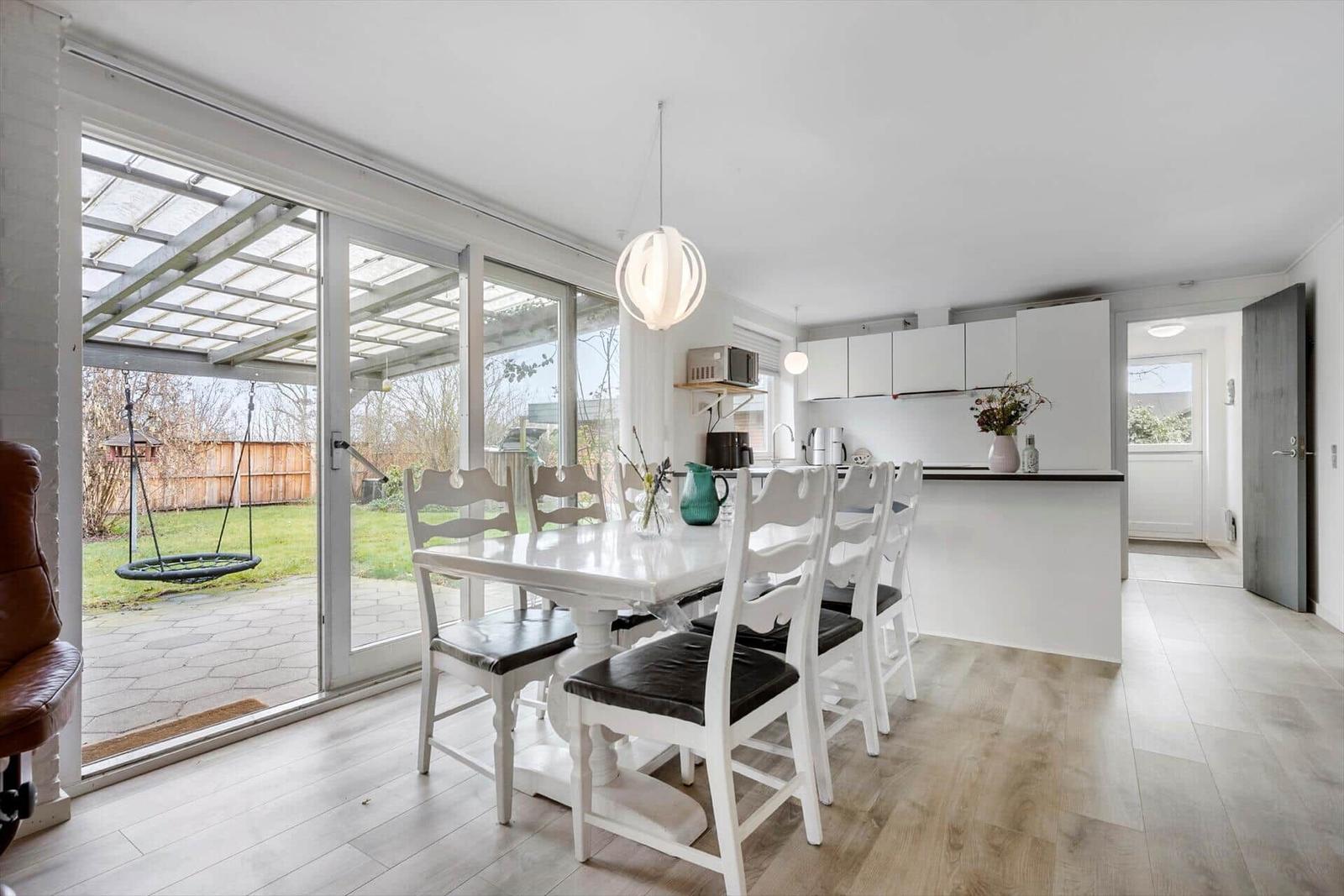 Dining area with table, chairs, and garden view. Kitchen with countertop and cabinets.