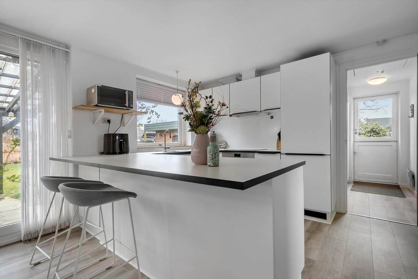 Modern kitchen with island, white cabinets, and view to the garden.