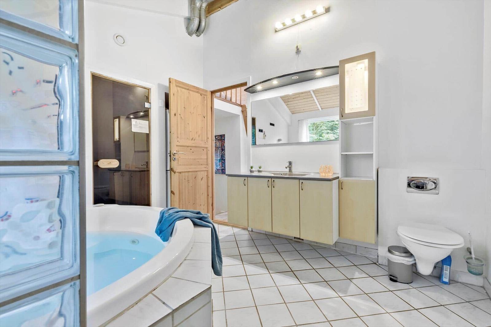Badezimmer mit Whirlpool, Waschbecken und Toilette. Holztür und Glaswand sichtbar.