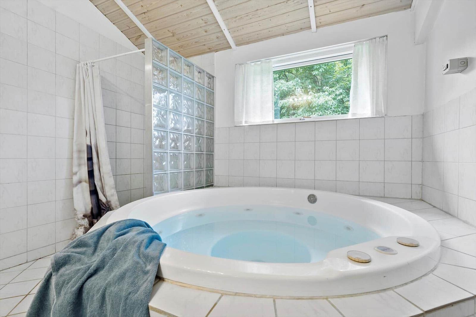 Whirlpool-Bad mit Glasblockwand und Fenster zur grünen Umgebung.