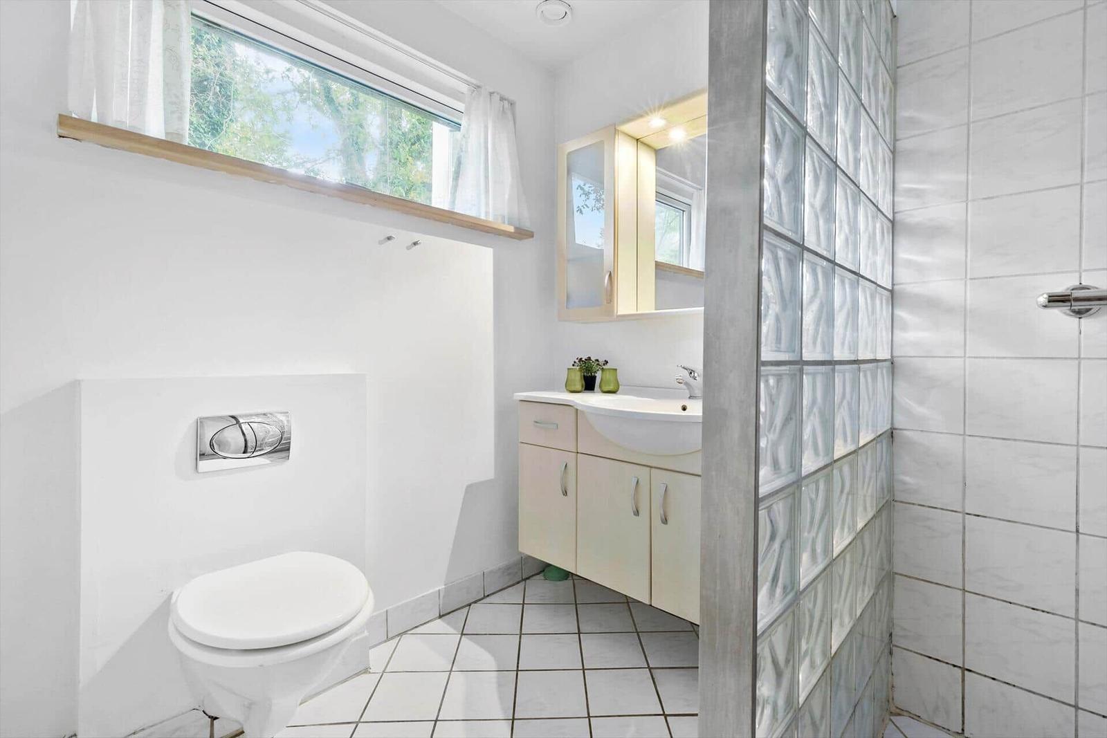 Badezimmer mit Toilette, Waschbecken und Dusche aus Glassteinen.