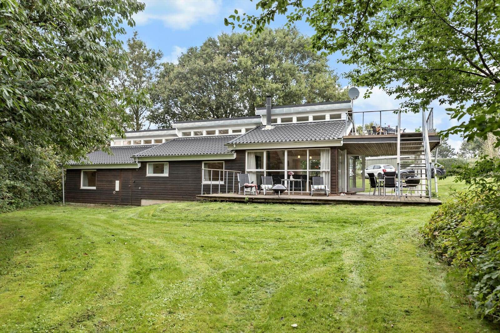 Moderne Villa mit Terrasse, Grill und Garten. Umgeben von Bäumen und Grünflächen.