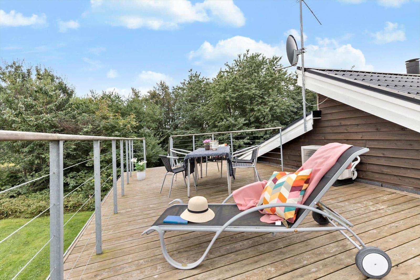 Terrasse mit Liegestuhl, Tisch und Stühlen, Blick auf Bäume und Himmel.