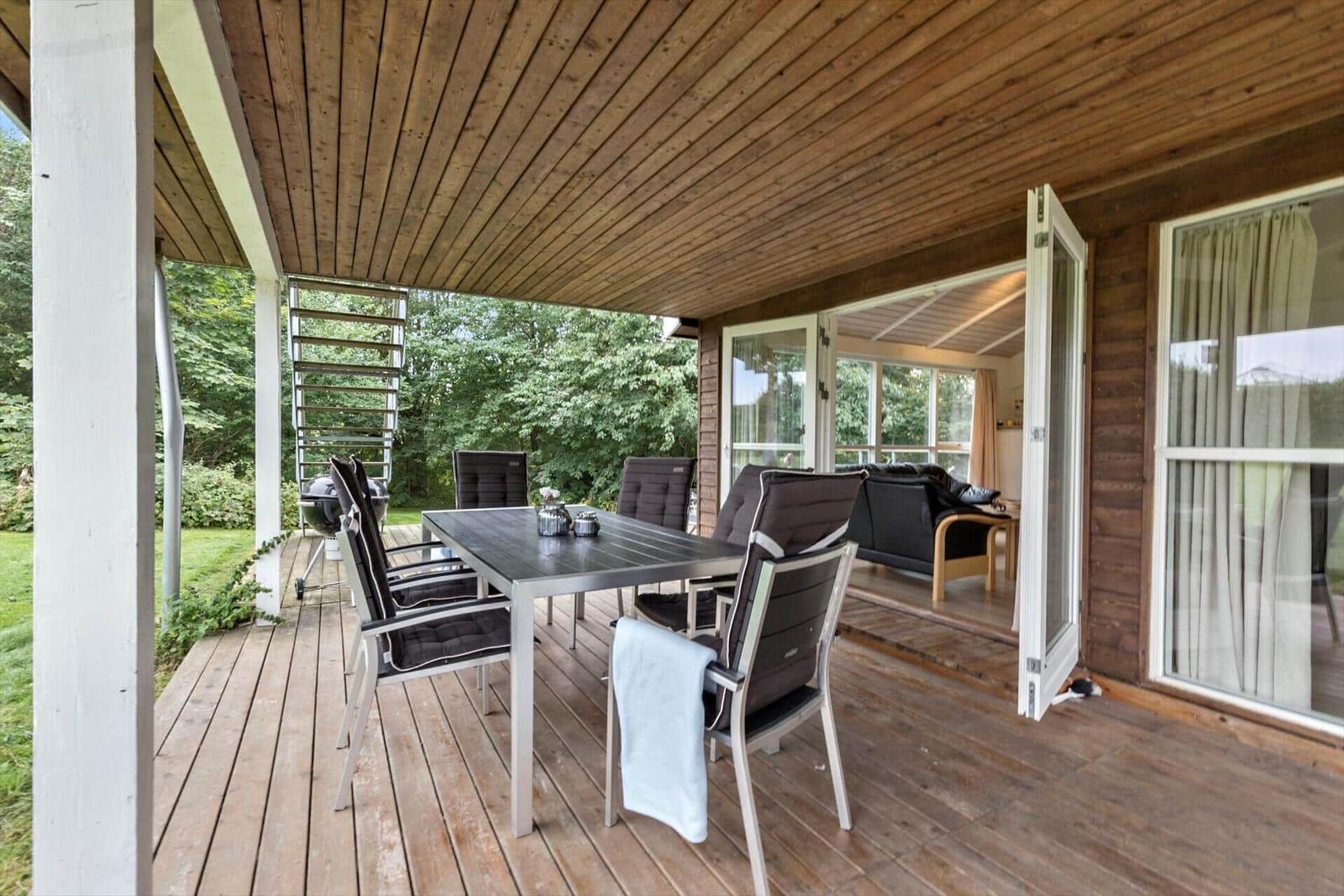 Terrasse mit Esstisch, Stühlen und Grill. Durchgehendes Holzgestühl und -decke.