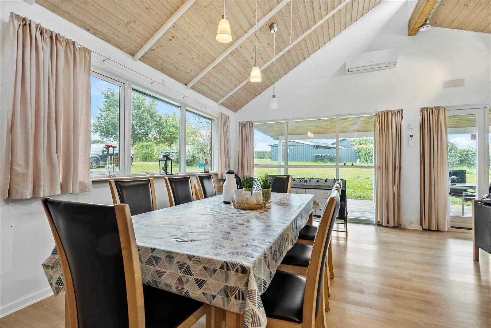 Esszimmer mit langem Tisch und Stühlen, großflächige Fenster und Holzdecke.