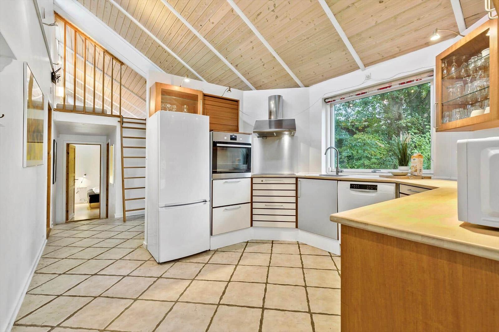 Küche mit Holzdecke, Kühlschrank, Backofen und Fenster mit Blick auf Grün.