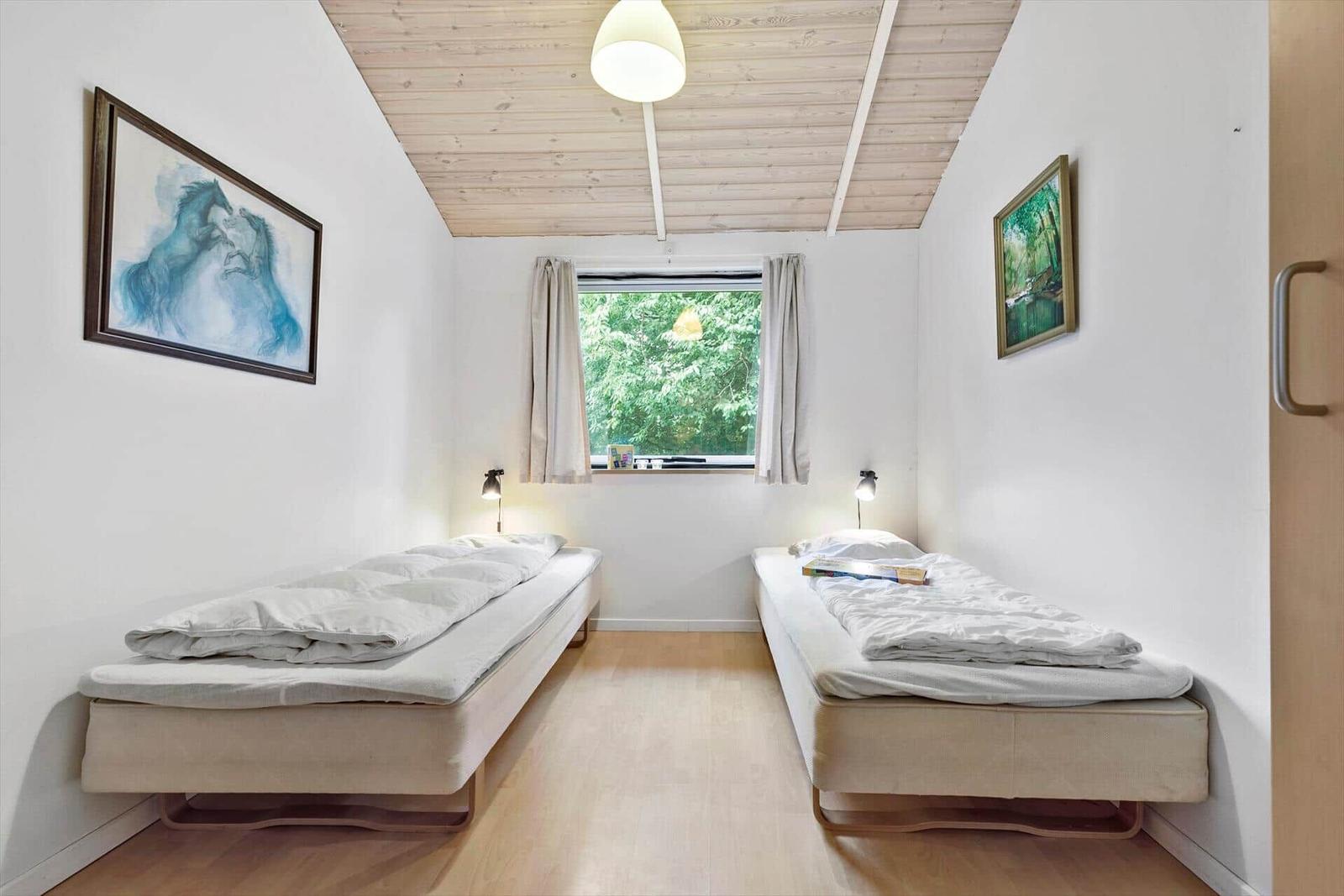 Zwei Einzelbetten in einem hellen Raum mit Holzboden und Fenster. Deckenbalken und Bilder an den Wänden.