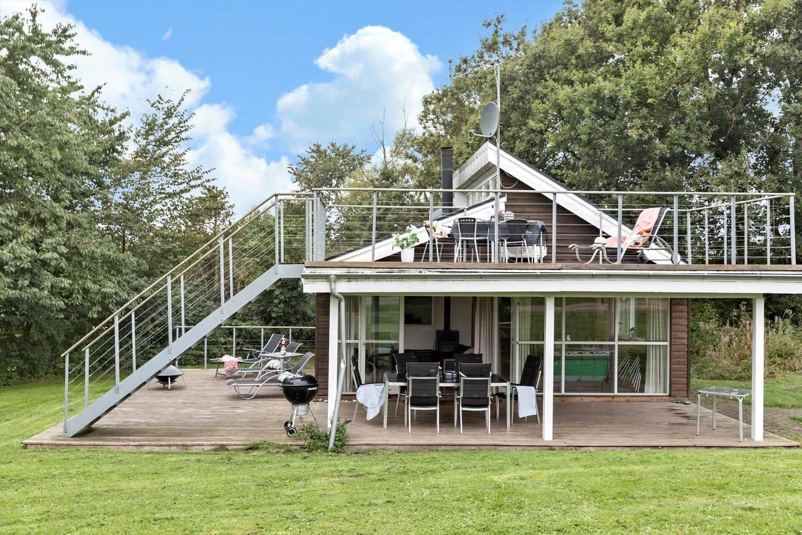 Haus mit Terrasse, Grill und Außensitzgelegenheiten in grüner Umgebung.