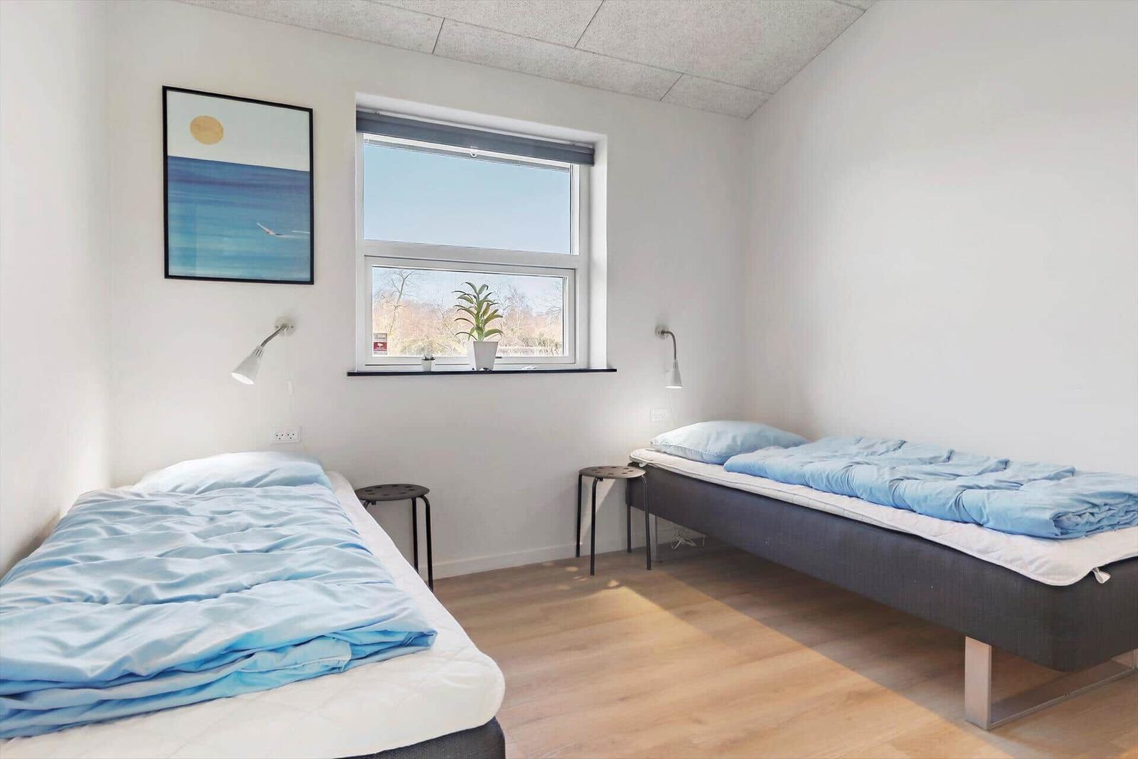 Zwei Betten mit blauen Decken, Fenster mit Pflanze und Wandbild.