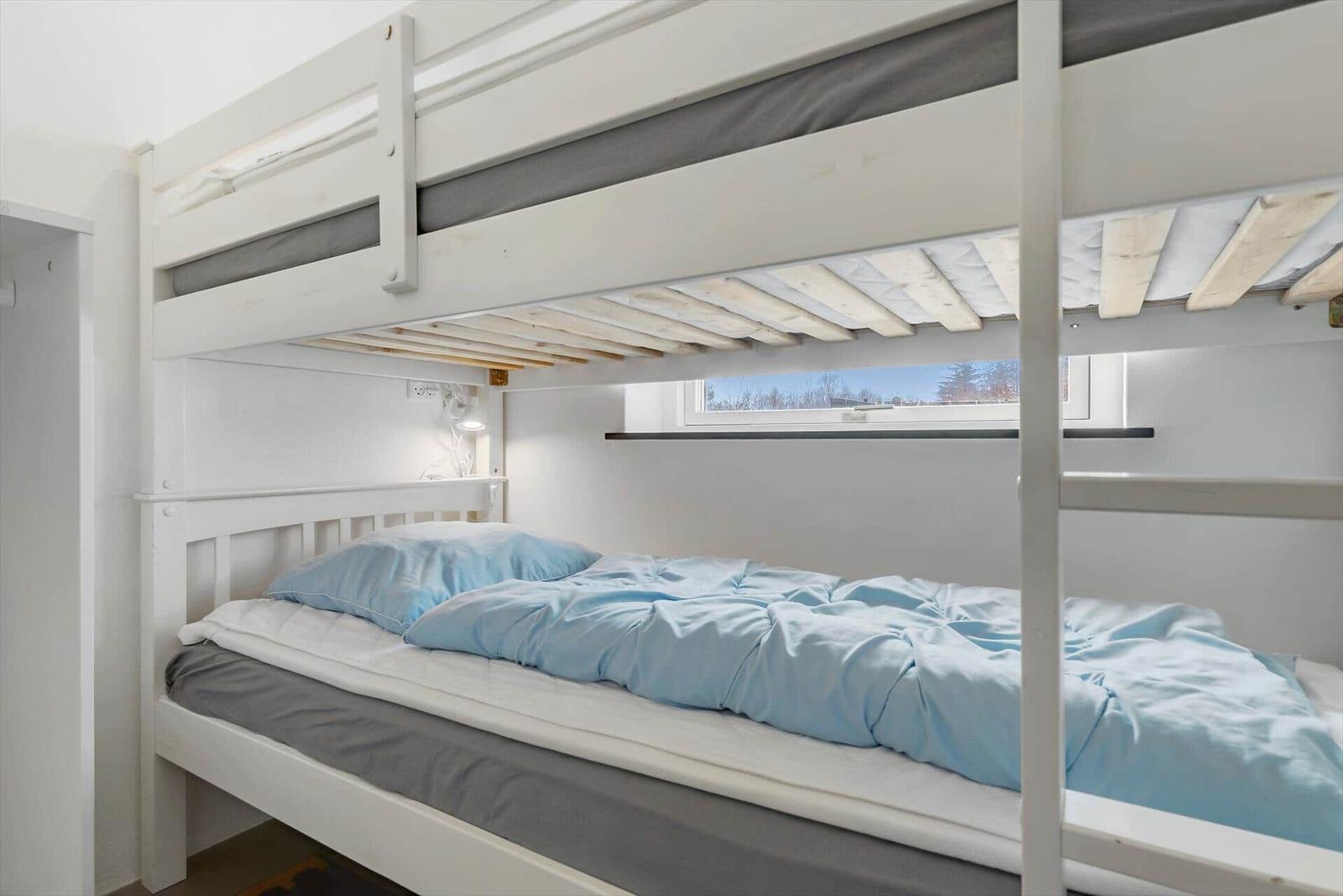 Doppelstockbett mit blauer Bettwäsche und kleinem Fenster.