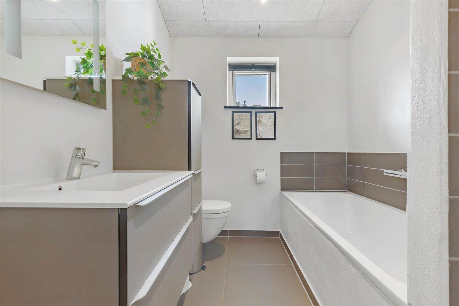 Badezimmer mit Badewanne, Waschbecken und Toilette. Fenster mit Bildern darüber.