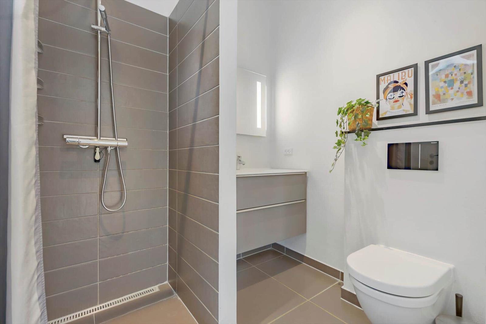 Badezimmer mit Dusche, Waschbecken und Toilette. Wandbild und Pflanze an der Wand.