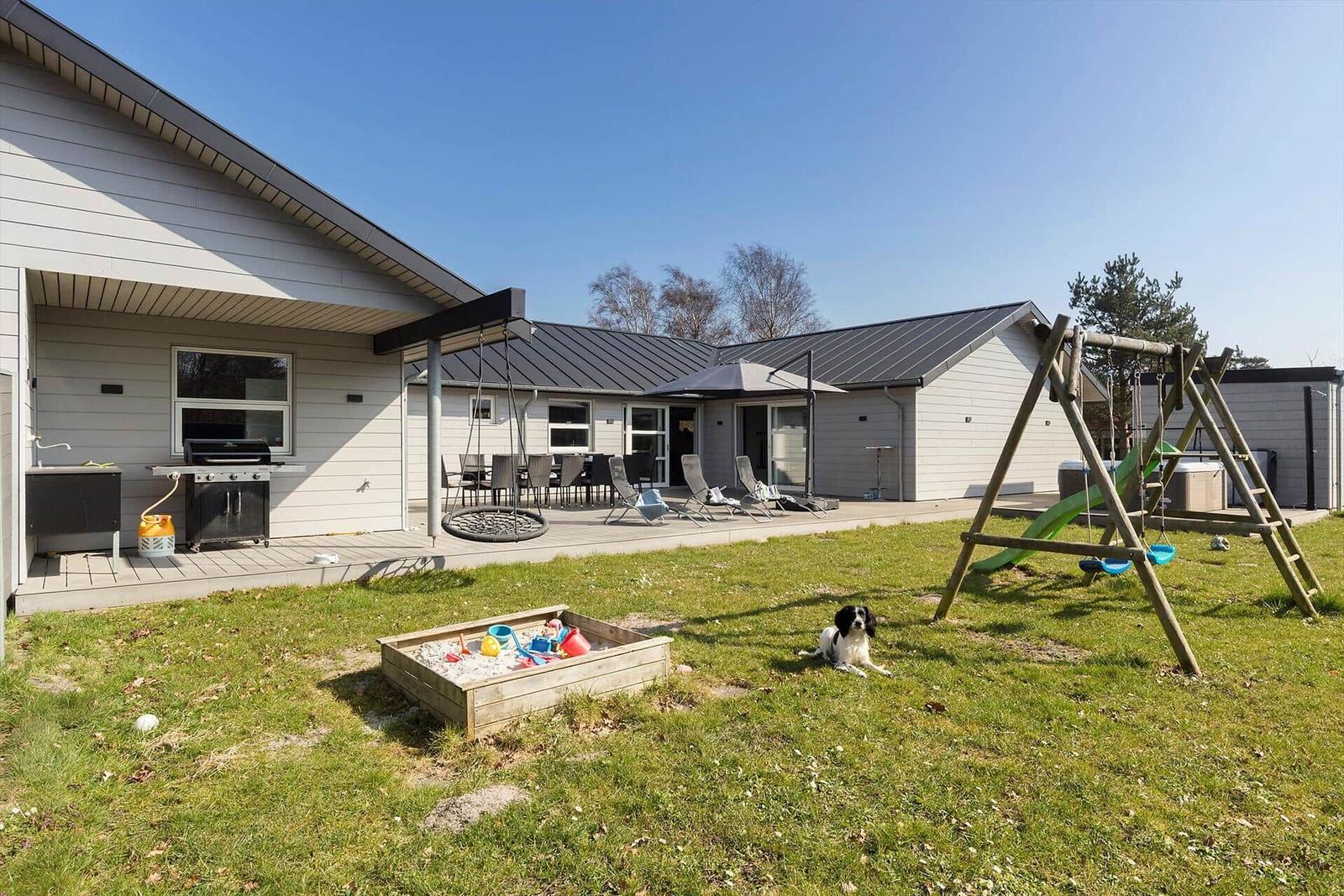 Haus mit Terrasse, Grill, Spielplatz und Hund auf dem Rasen.