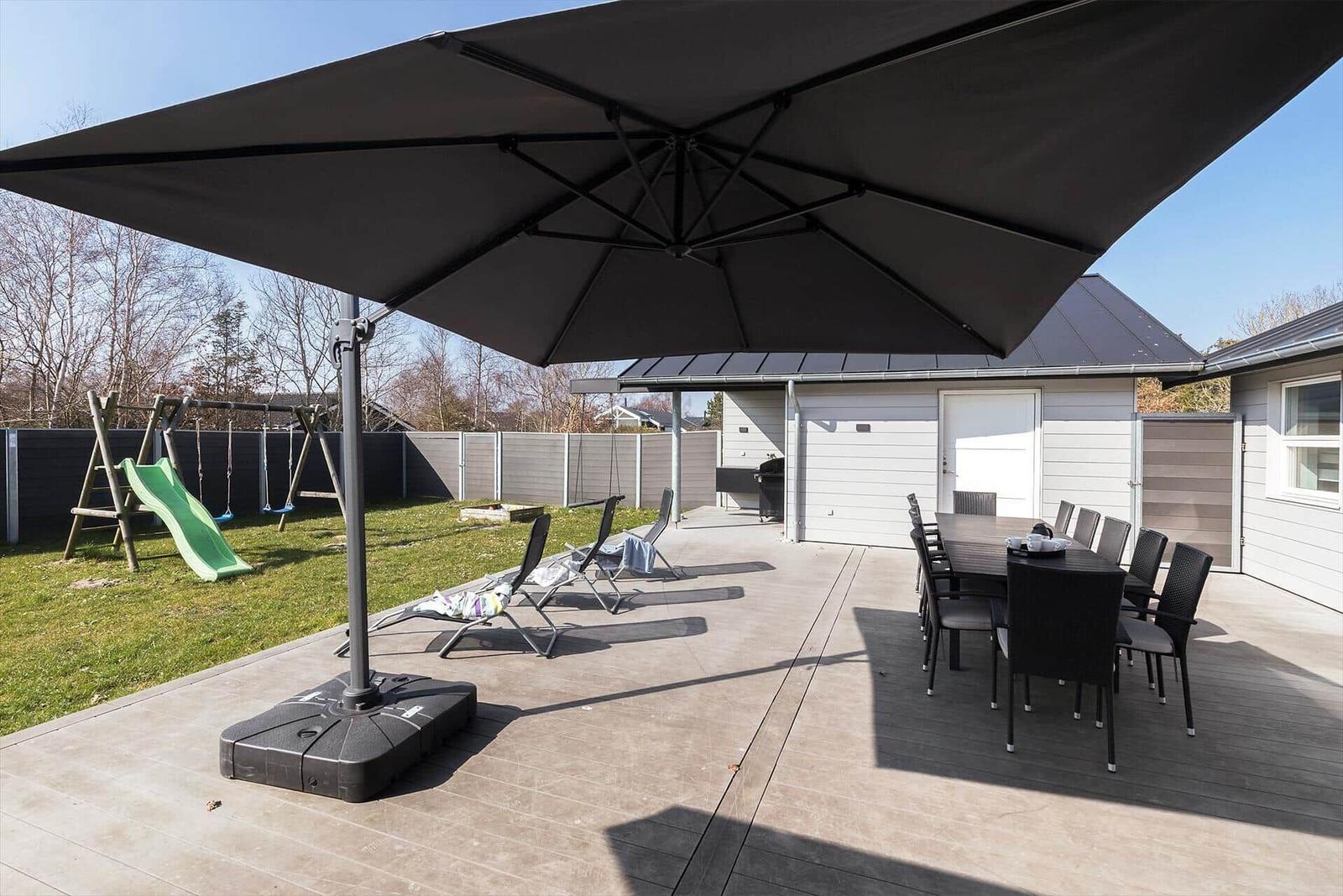 Großer Gartenbereich mit Sonnenschirm, Sitzgruppe und Spielplatz.