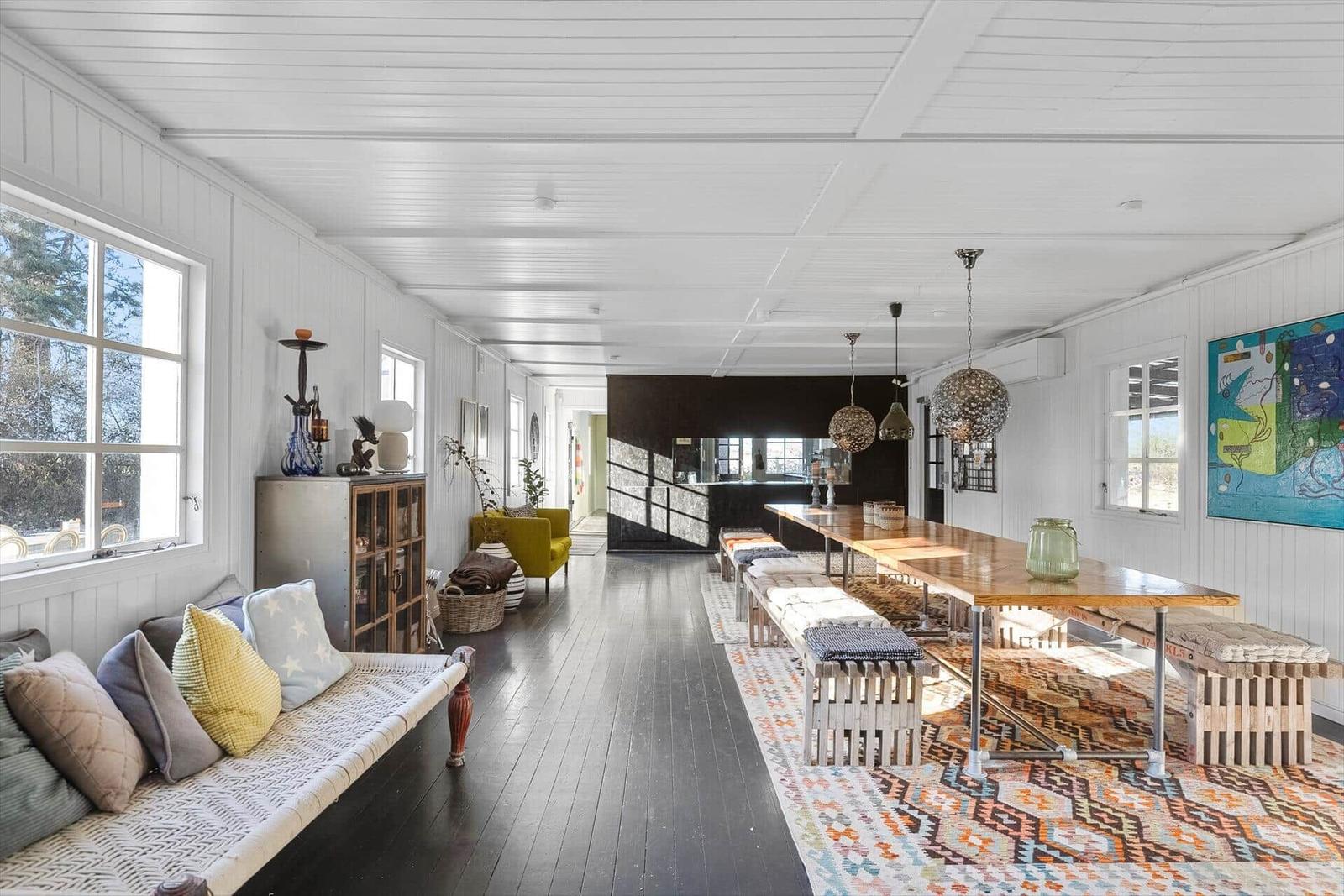 Lang gezogener Raum mit Holzboden, Sofa, Esstisch und Wandbild.