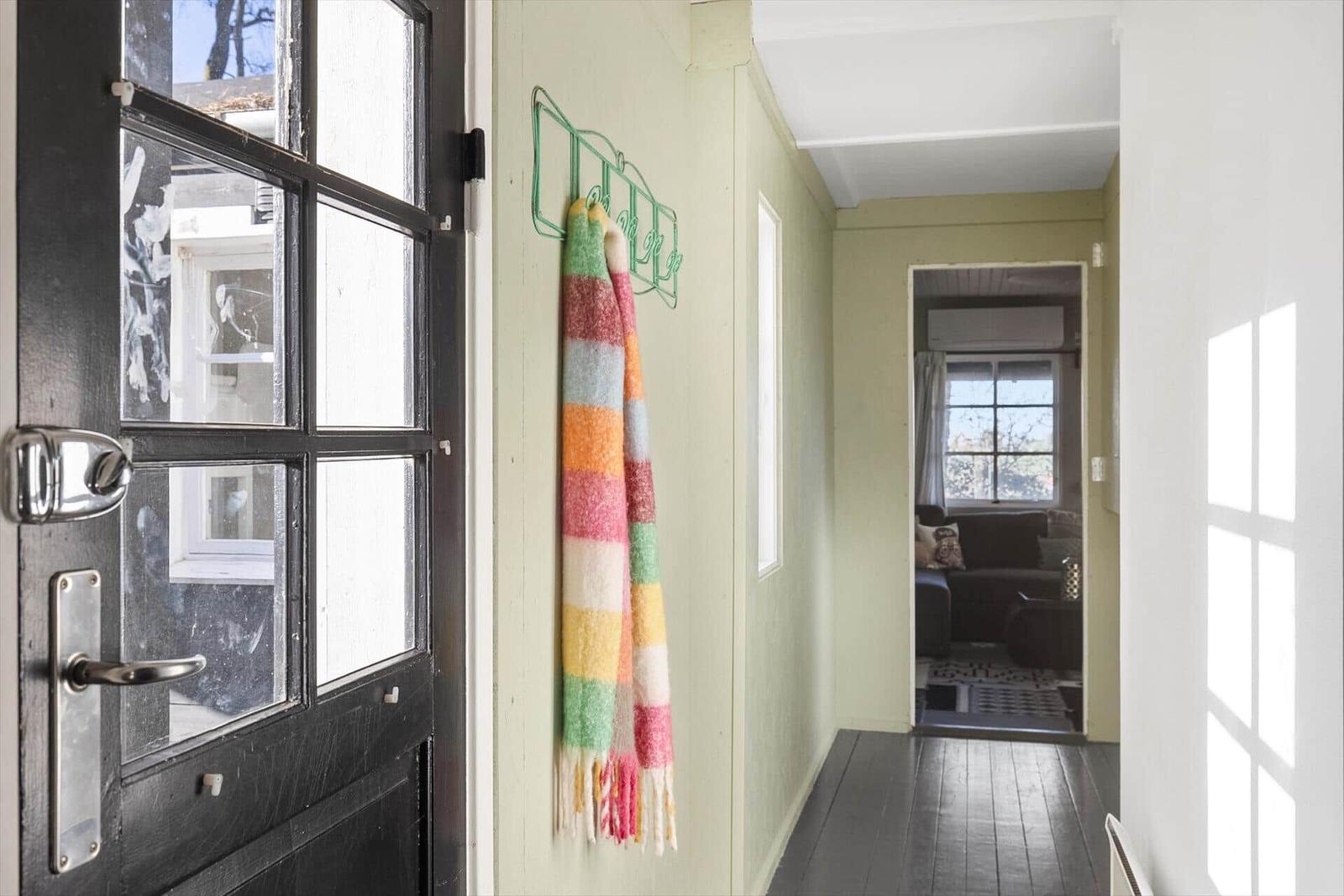 Eingangsbereich mit schwarzer Tür und buntem Schal an der Wand. Durchgang zu Wohnzimmer mit Sofa.