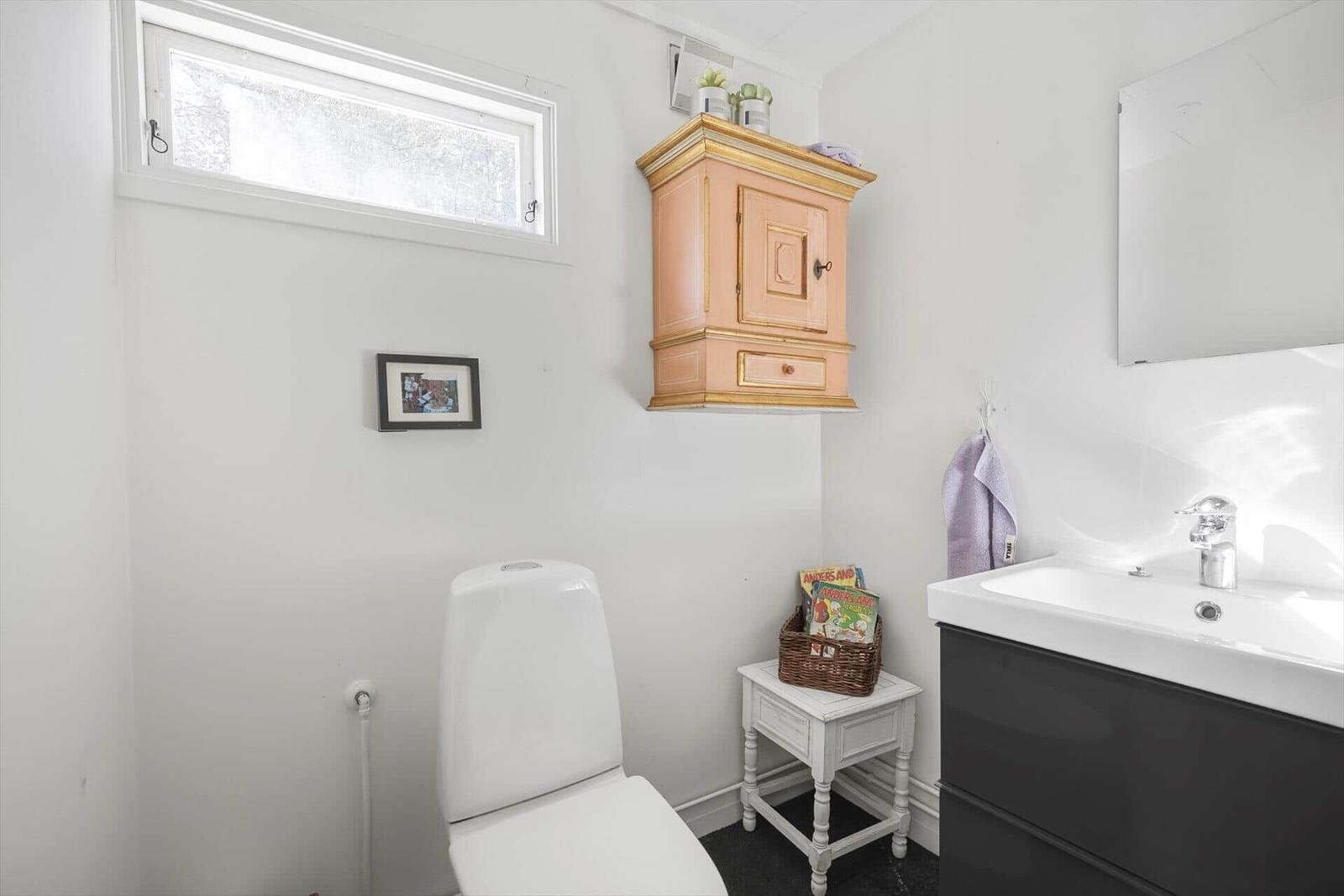 Badezimmer mit Toilette, Waschbecken und Holzschrank.