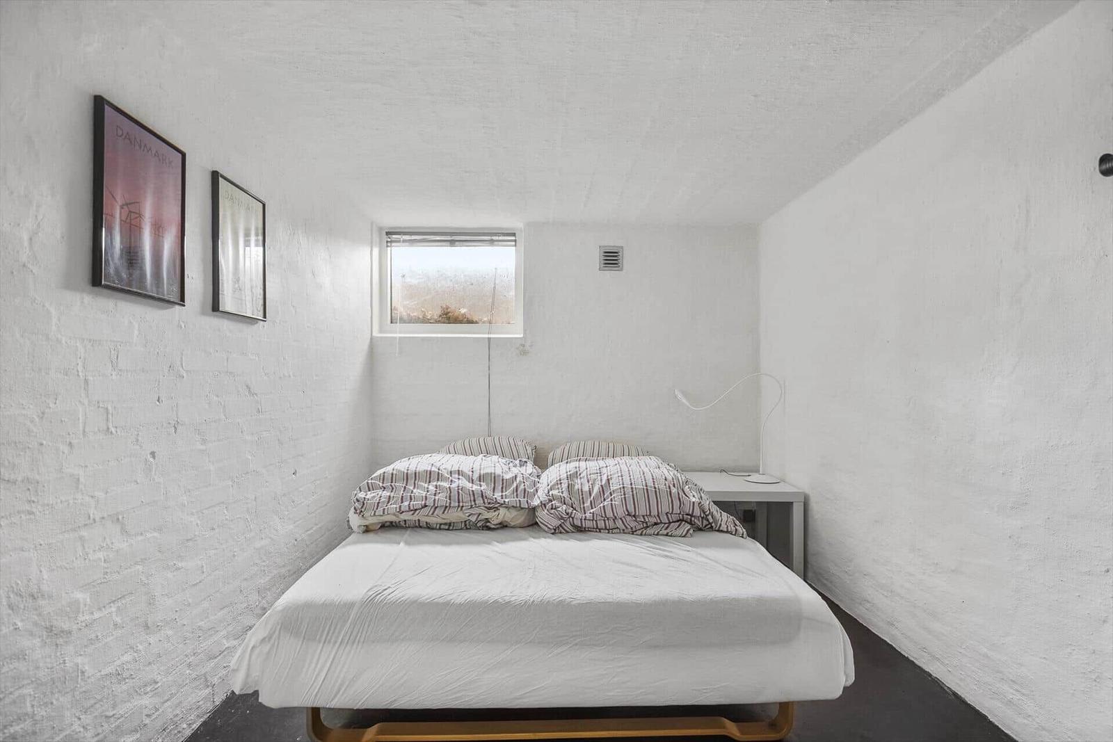 Schlafzimmer mit Bett, Fenster und Wandbildern.