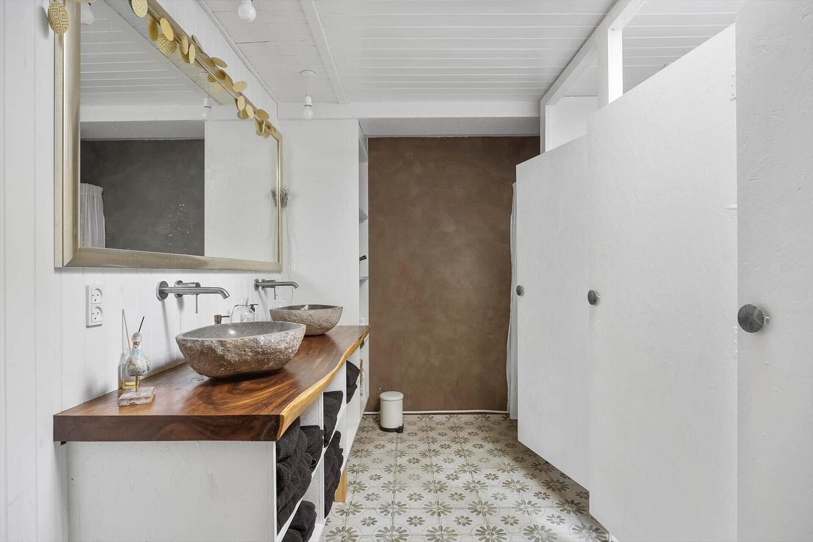 Badezimmer mit Steinwaschbecken, Holzwaschtisch und floraler Fliesenboden.
