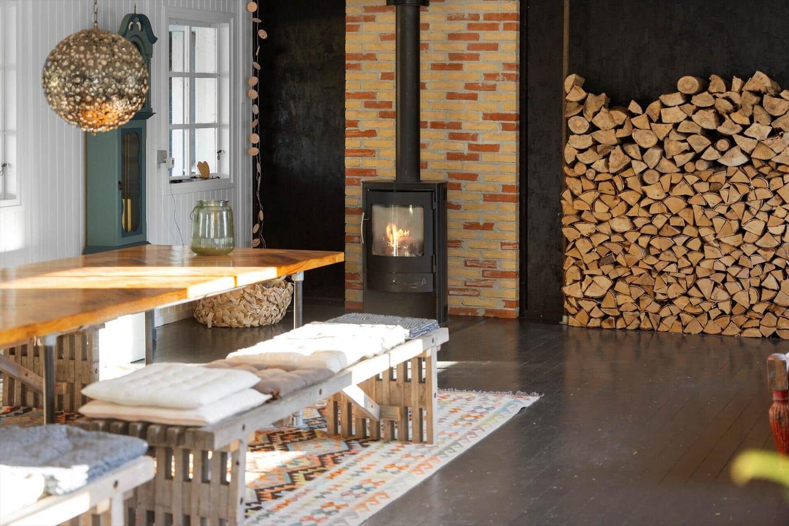 Raum mit Holzofen, Holzstapel und Holztisch mit Sitzbank.