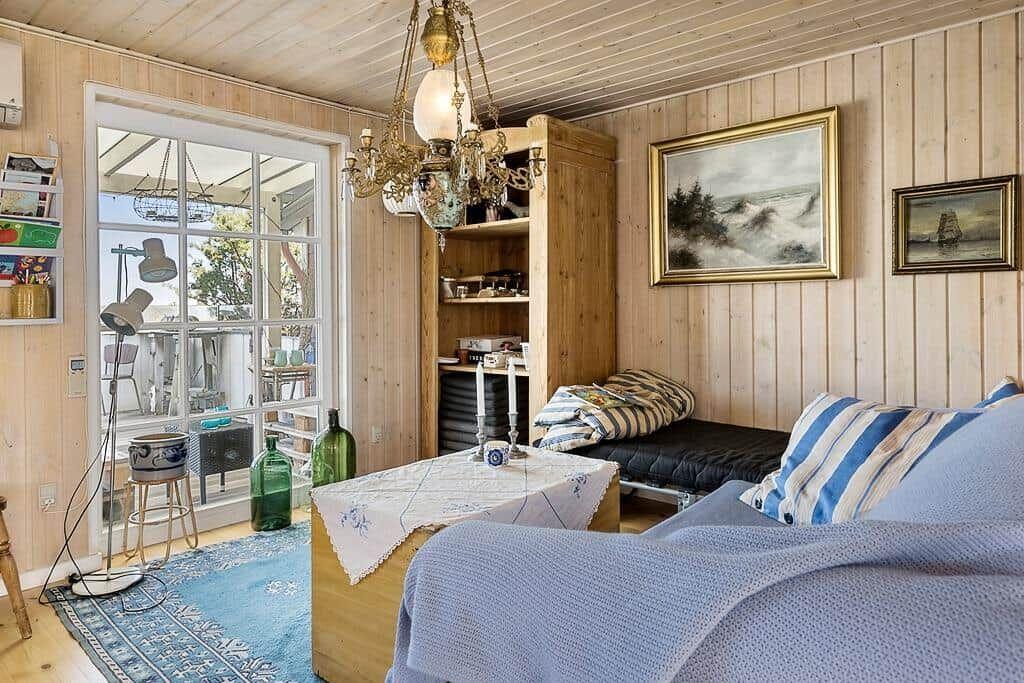 Wohnraum mit Holzwand, Sofa, Tisch und Fenster zur Terrasse.