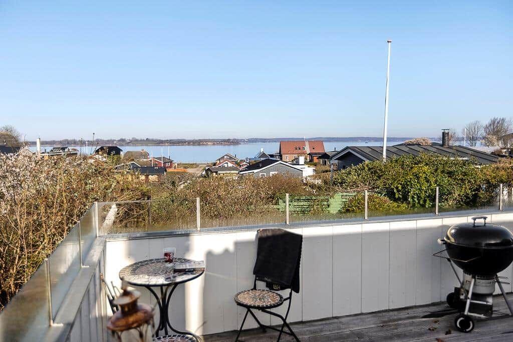 Terrasse mit Tisch, Stuhl und Grill. Blick auf Wasser und Häuser.