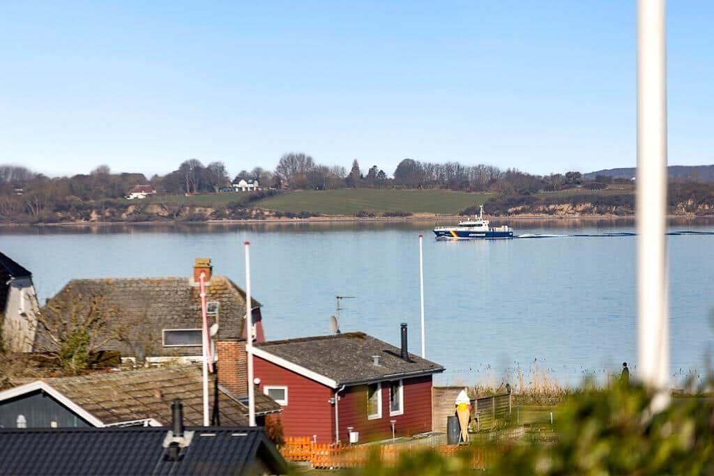 Boot fährt auf dem Wasser, Häuser und Hügel im Hintergrund.
